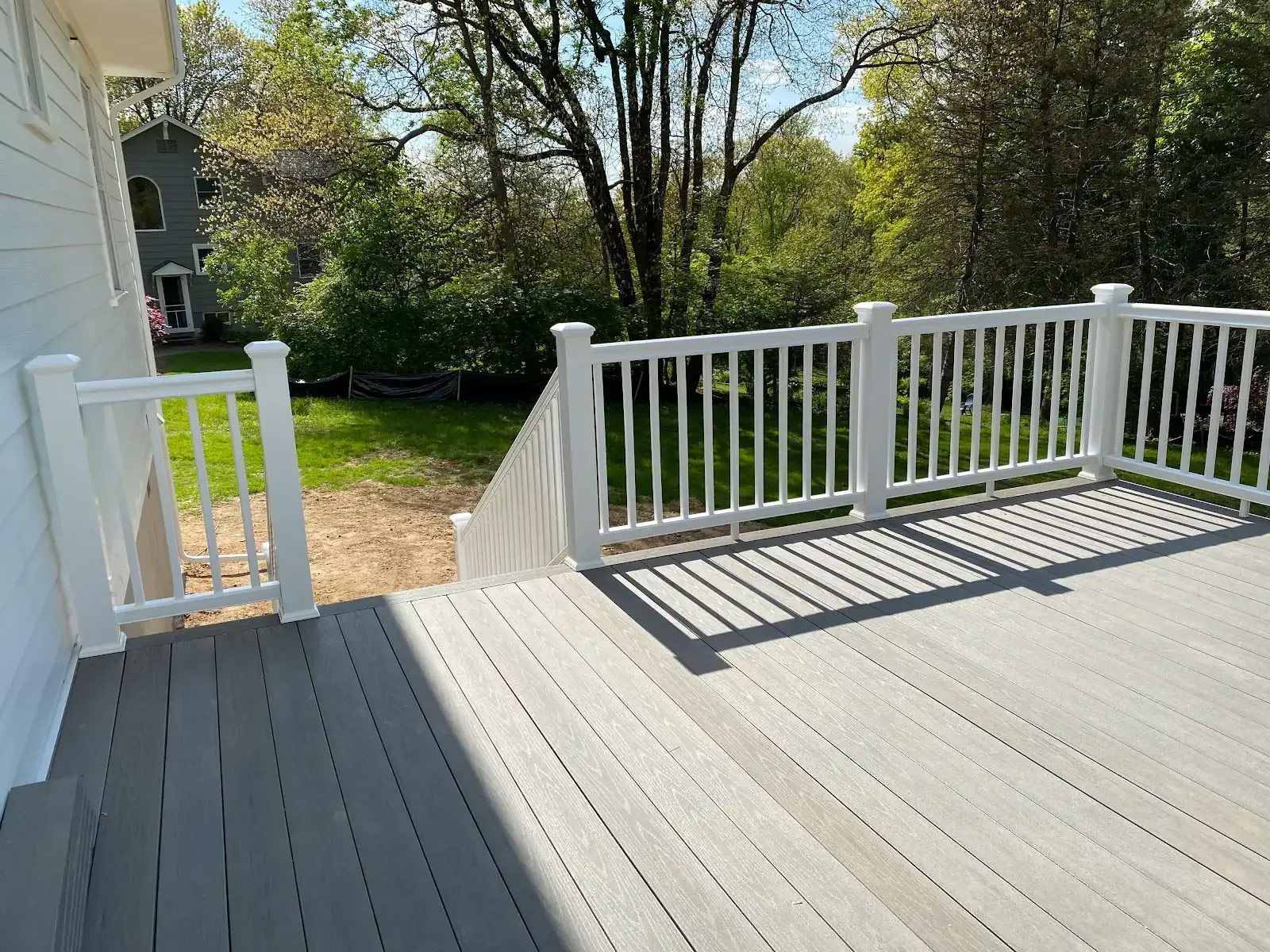 A gray deck with a white railing and trees in the background
