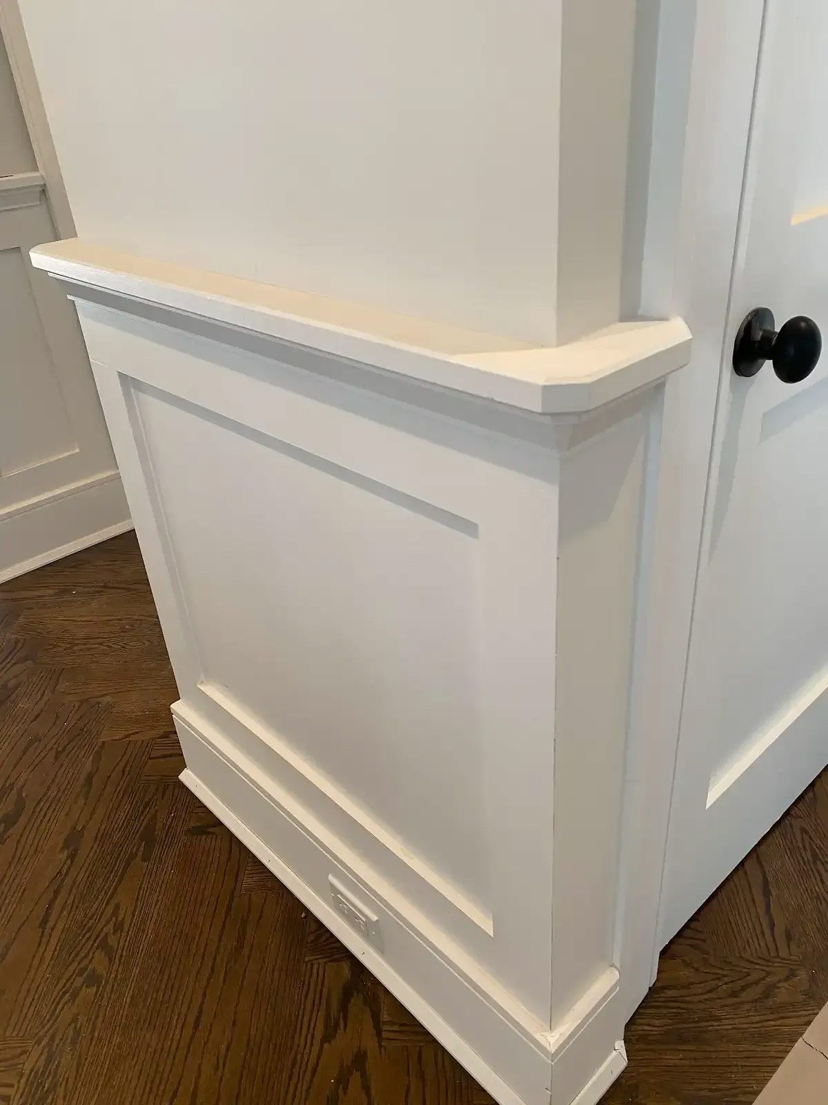 A close up of a white cabinet with black knobs on a wooden floor