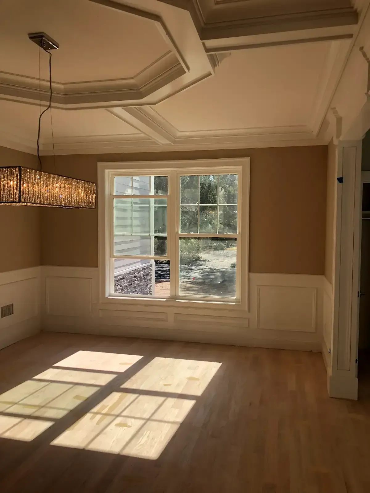 An empty dining room with a large window and a chandelier