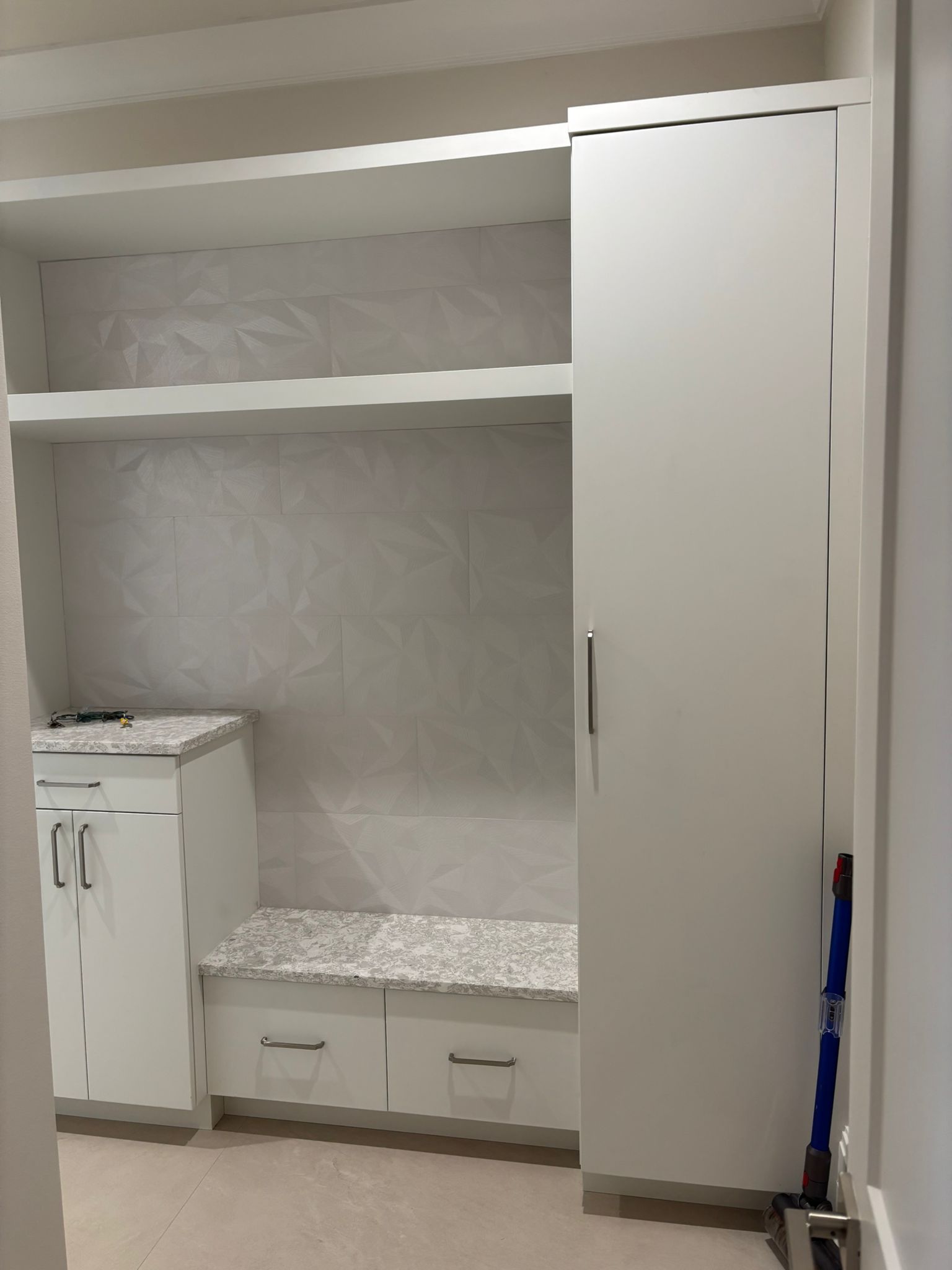 A room with white cabinets, shelves, drawers and a bench