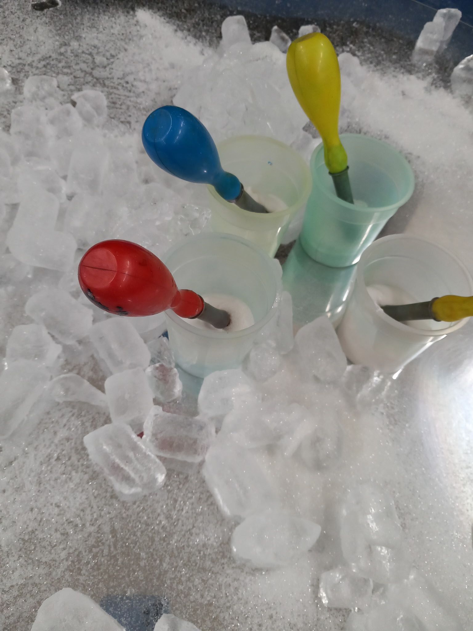 Three plastic cups with colorful spoons in ice.