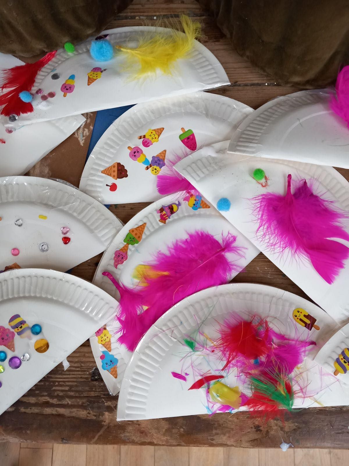 Decorated paper plates with feathers, stickers, and other craft materials, likely for a children's project.