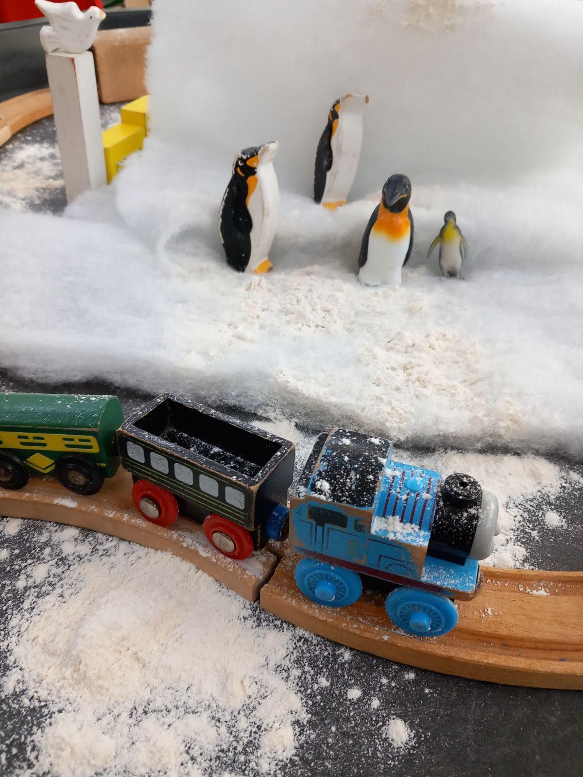Toy train on tracks near penguins in a snowy scene.