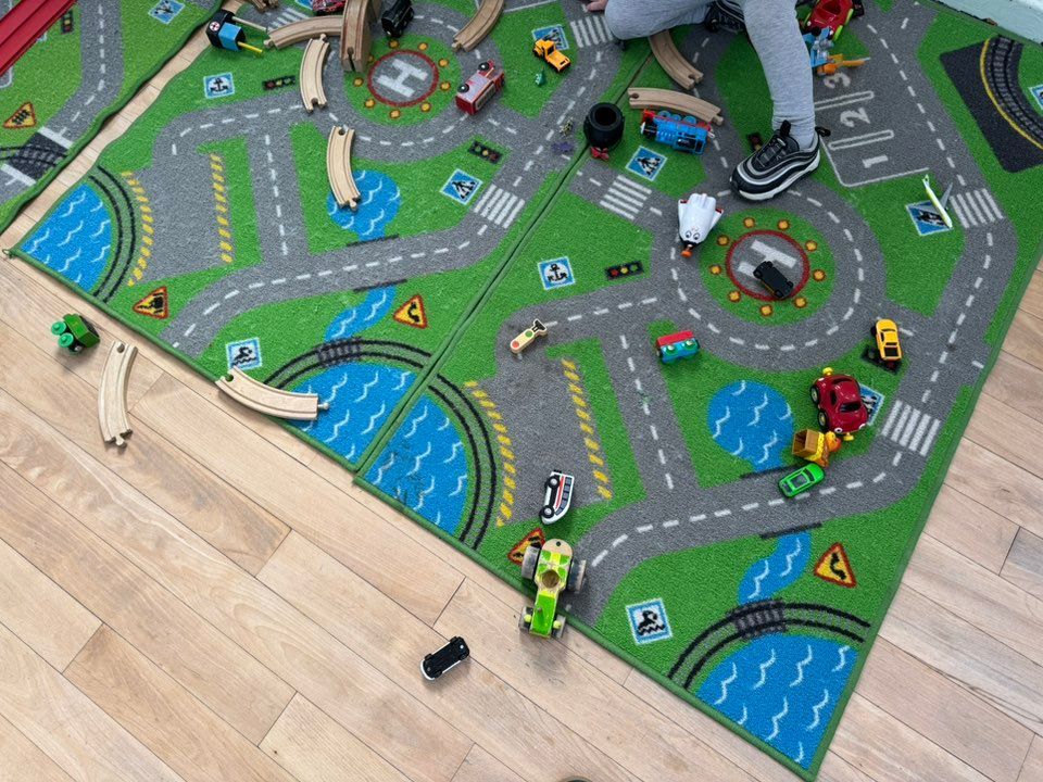 Child playing with toy cars and train set on a road-themed play mat.