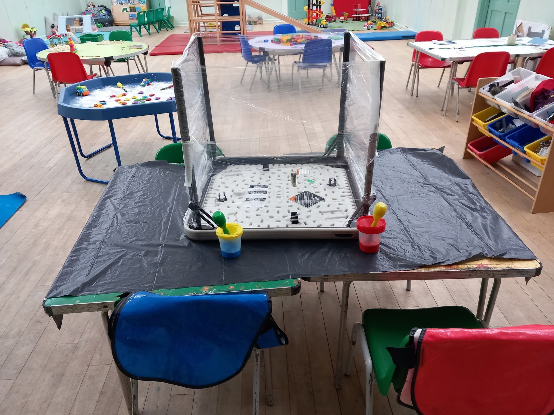 A child's play area with a table covered in black plastic and a play structure. Chairs are nearby.