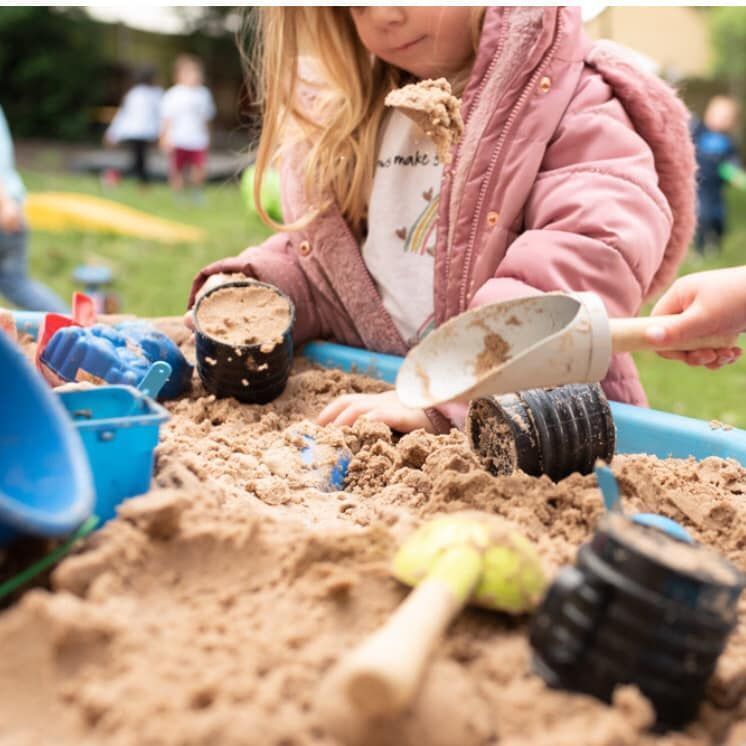 Child playing in a sandbox with sand tools, wearing a pink coat.