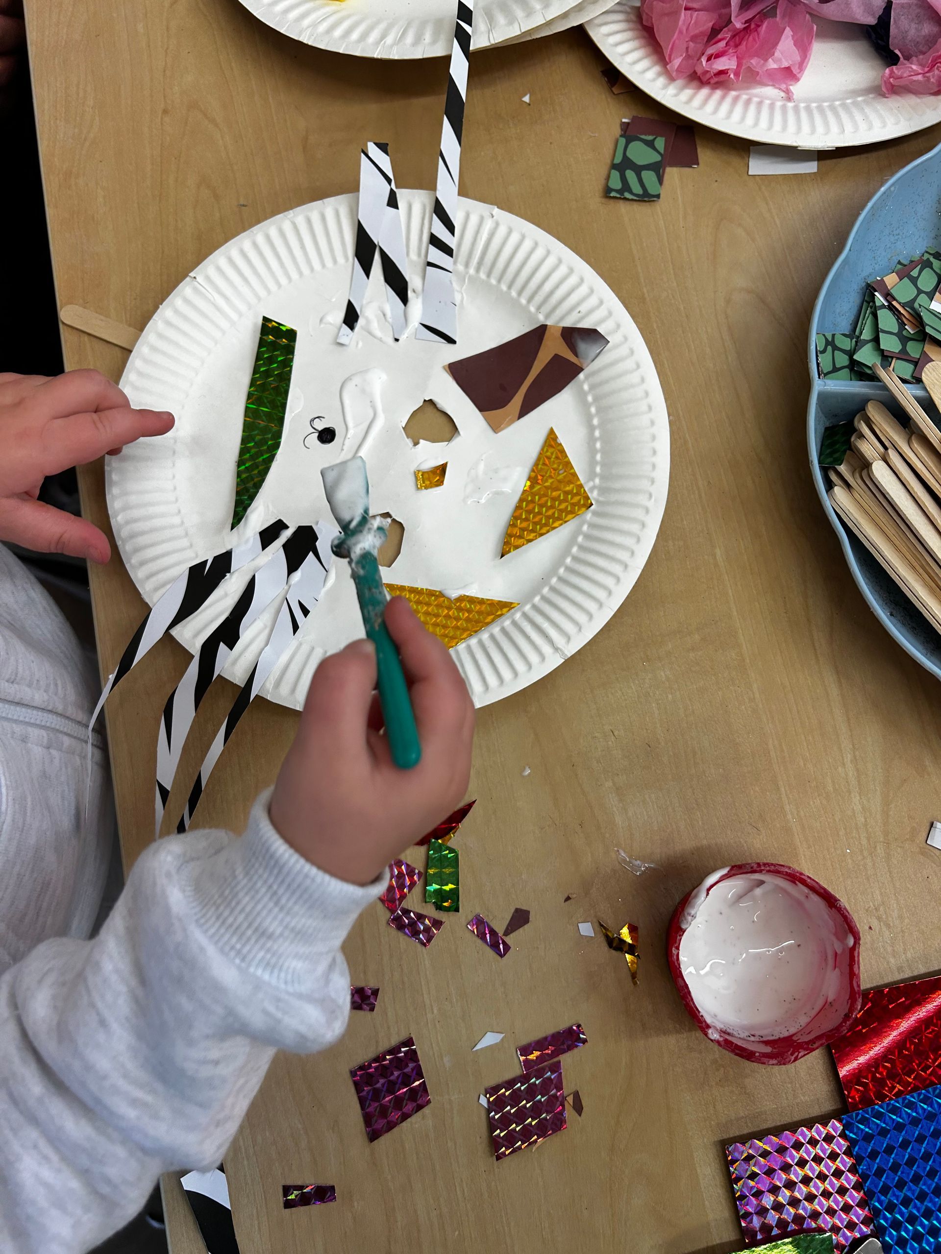 Child gluing colorful paper shapes to a paper plate; craft activity.