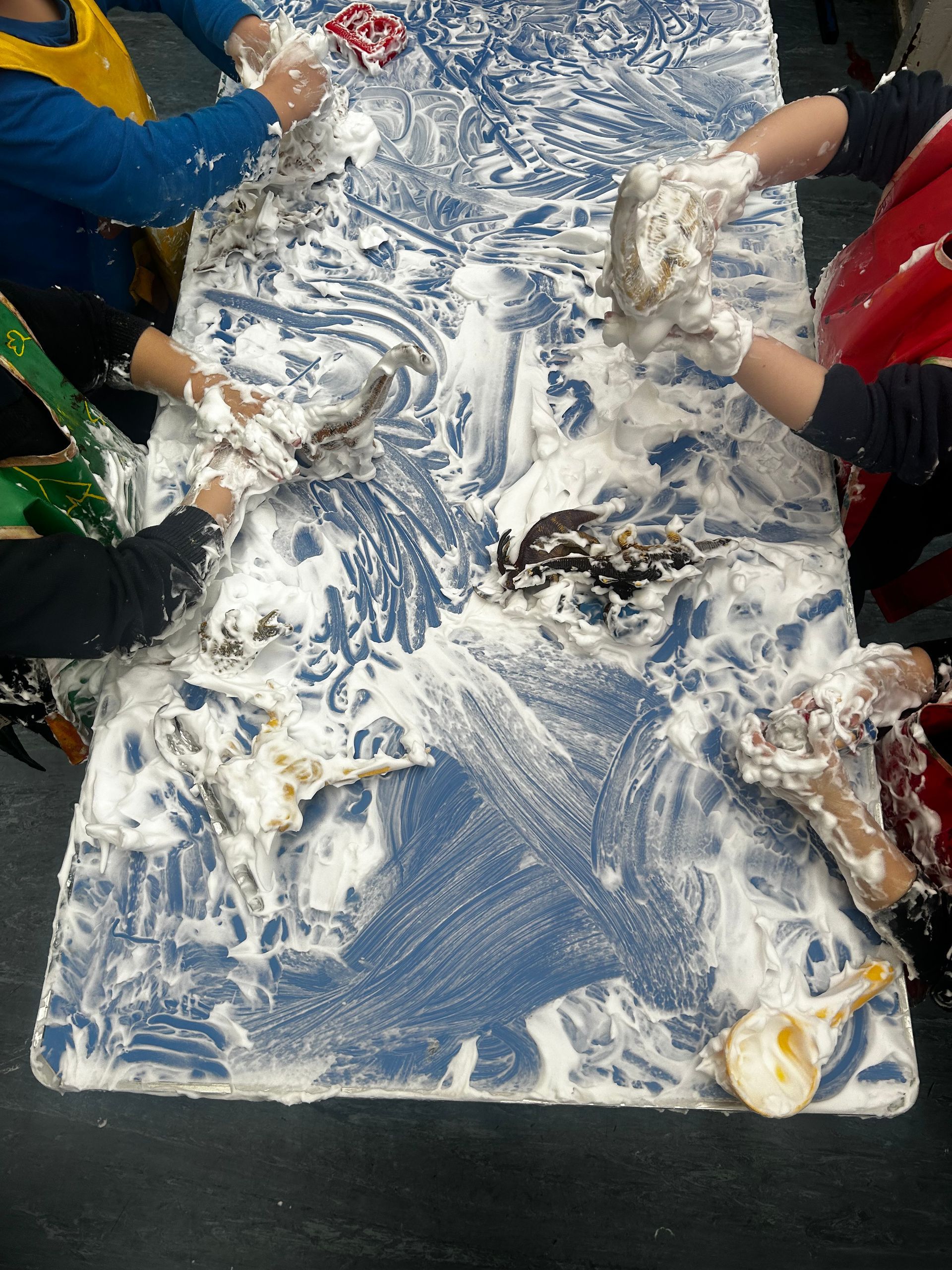 Children's hands covered in white foam spread across a blue table.