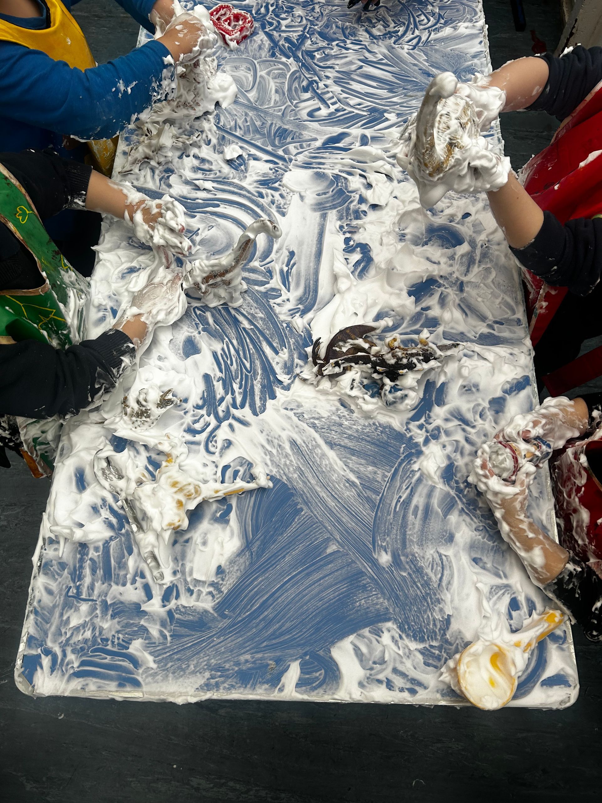 Children's hands covered in white foam on a blue table.