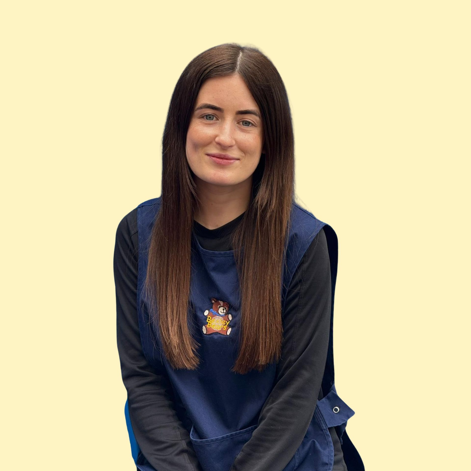 Blonde woman smiling broadly against a yellow background, wearing a white top.