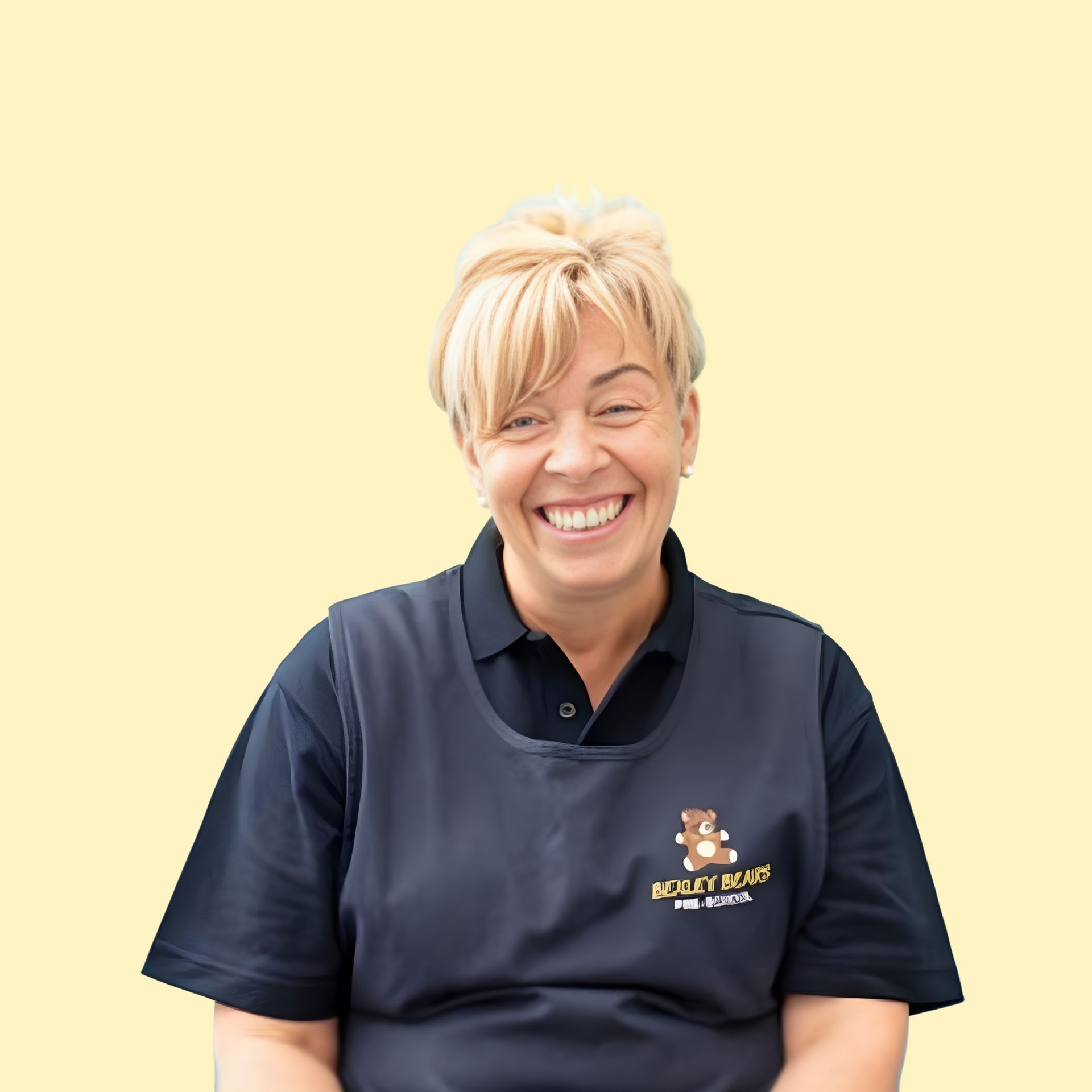 Blonde woman smiling broadly against a yellow background, wearing a white top.