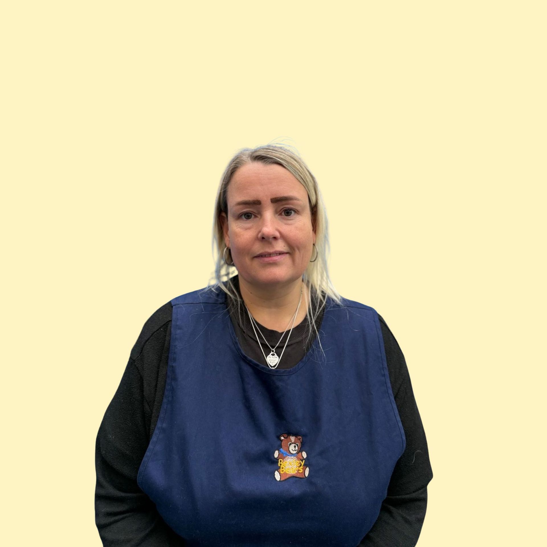 Blonde woman smiling broadly against a yellow background, wearing a white top.