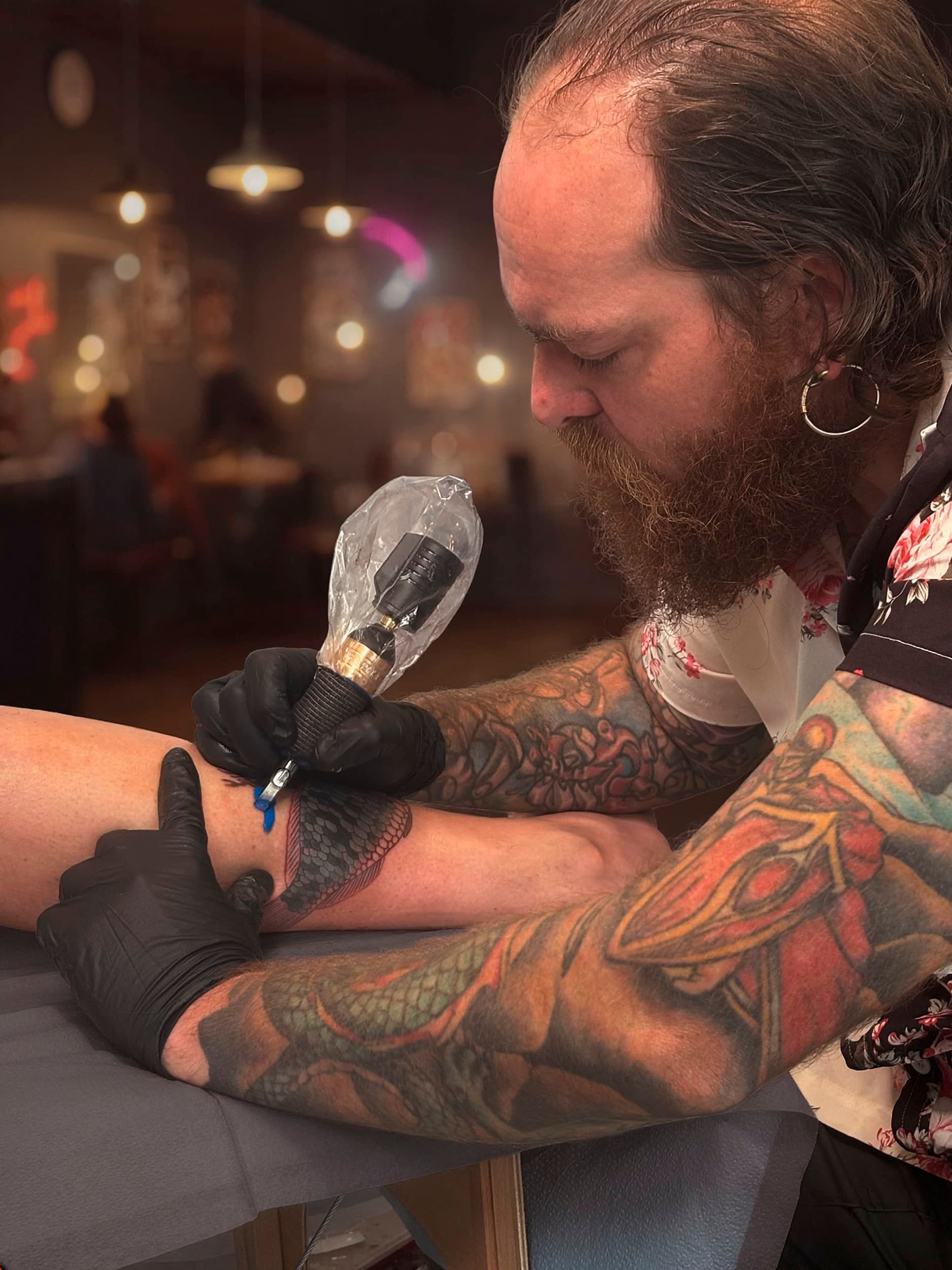 Tattoo artist using a machine to tattoo a person’s forearm in a dim studio