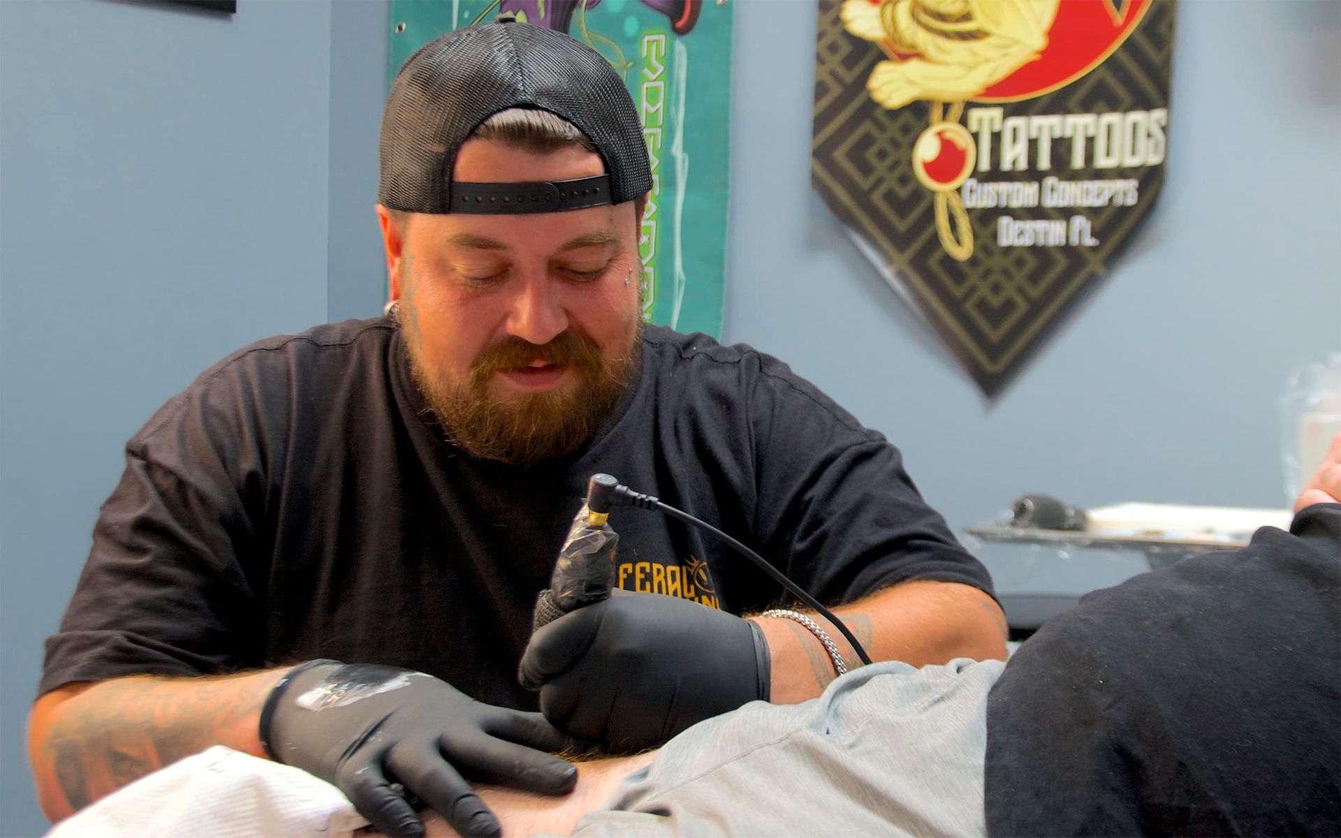Tattoo artist in black gloves working on a client’s arm in a tattoo studio