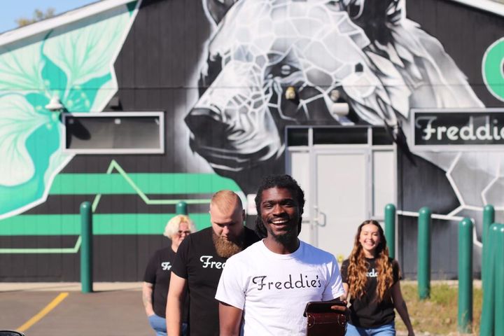 A group of people are standing in front of a mural of a bear with the name freddie on it