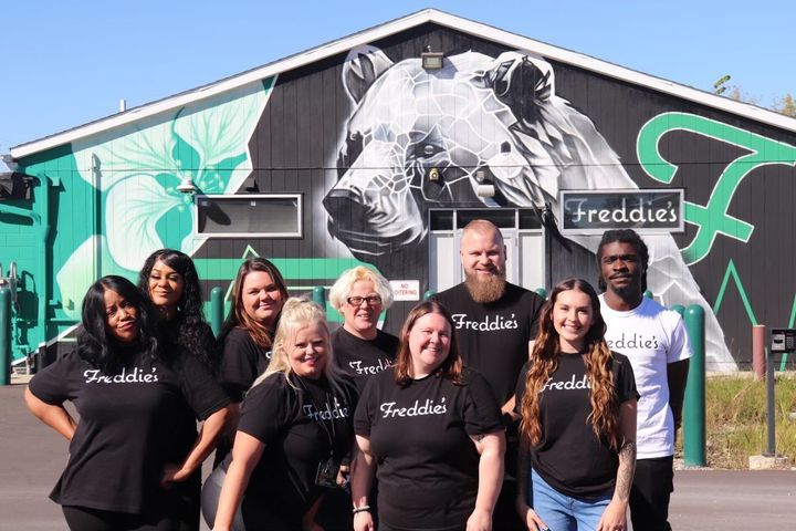 A group of people are posing for a picture in front of a building with a mural of a bear on it.