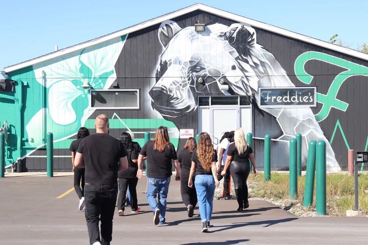 A group of people are walking in front of a building with a mural of a bear on it.