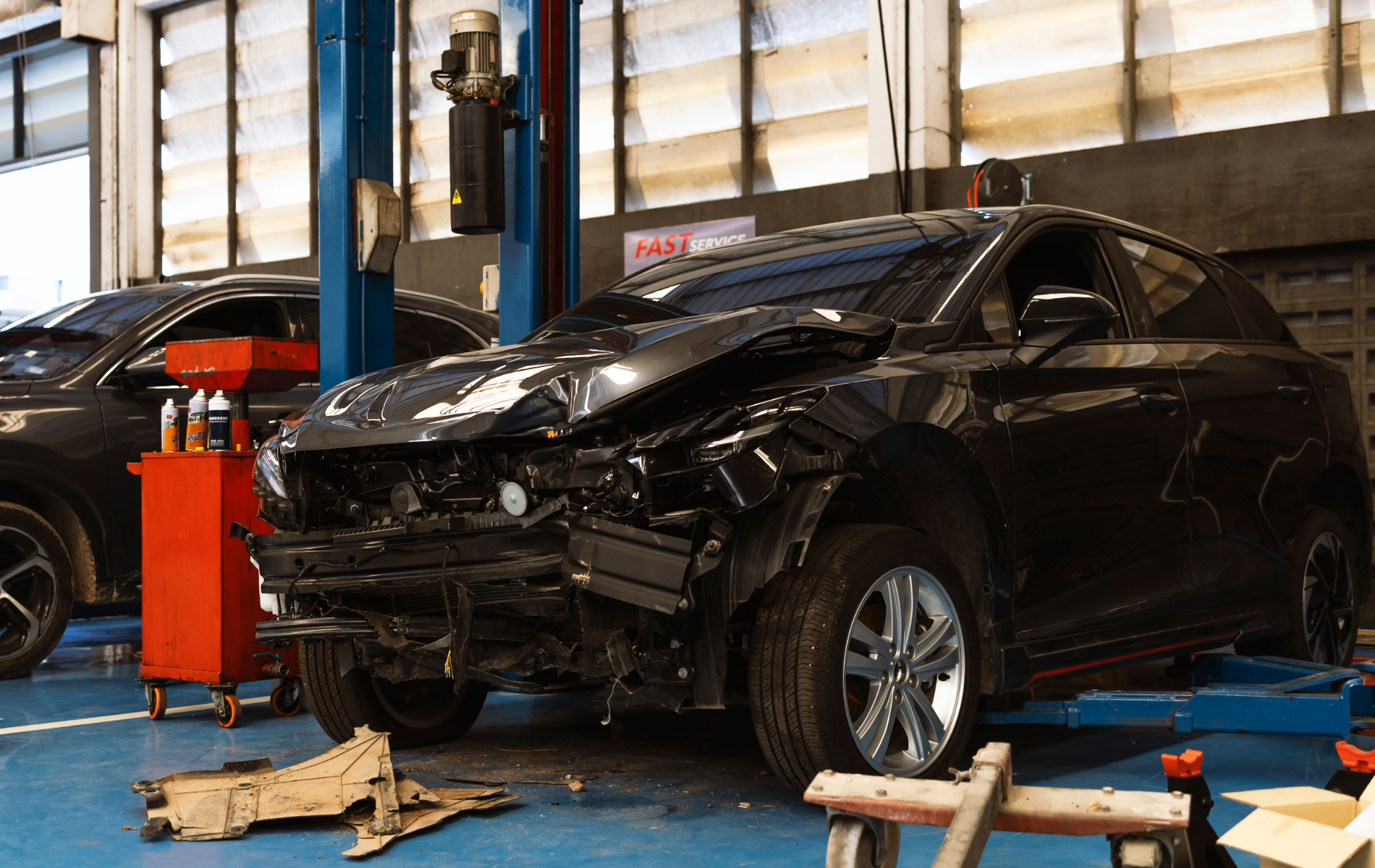 A black car with front-end collision damage parked in a bright auto repair shop.