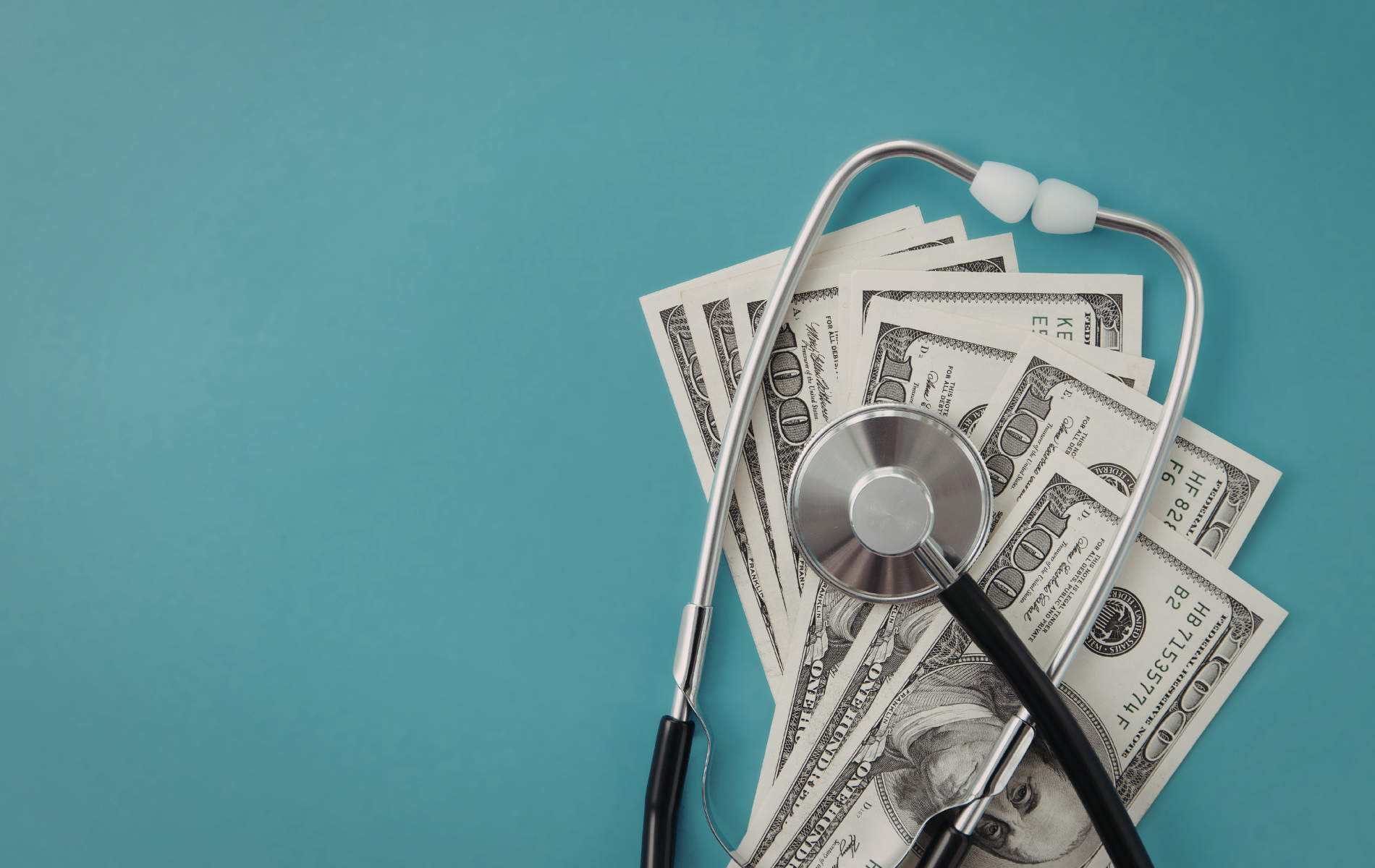 A medical stethoscope rests on a small stack of US one-hundred-dollar bills against a plain teal background.