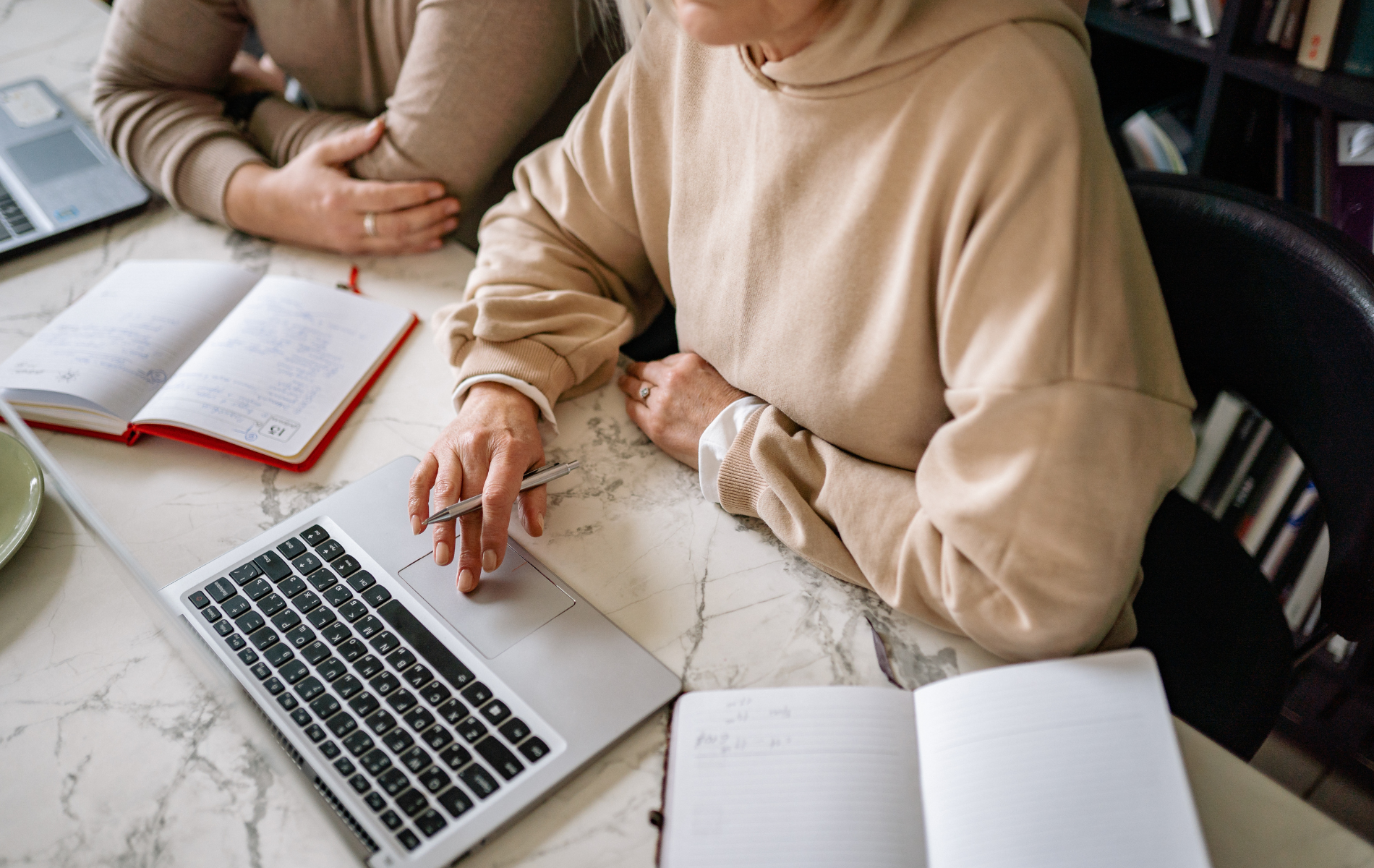 Two people sit at a white marble desk working with laptops and notebooks.