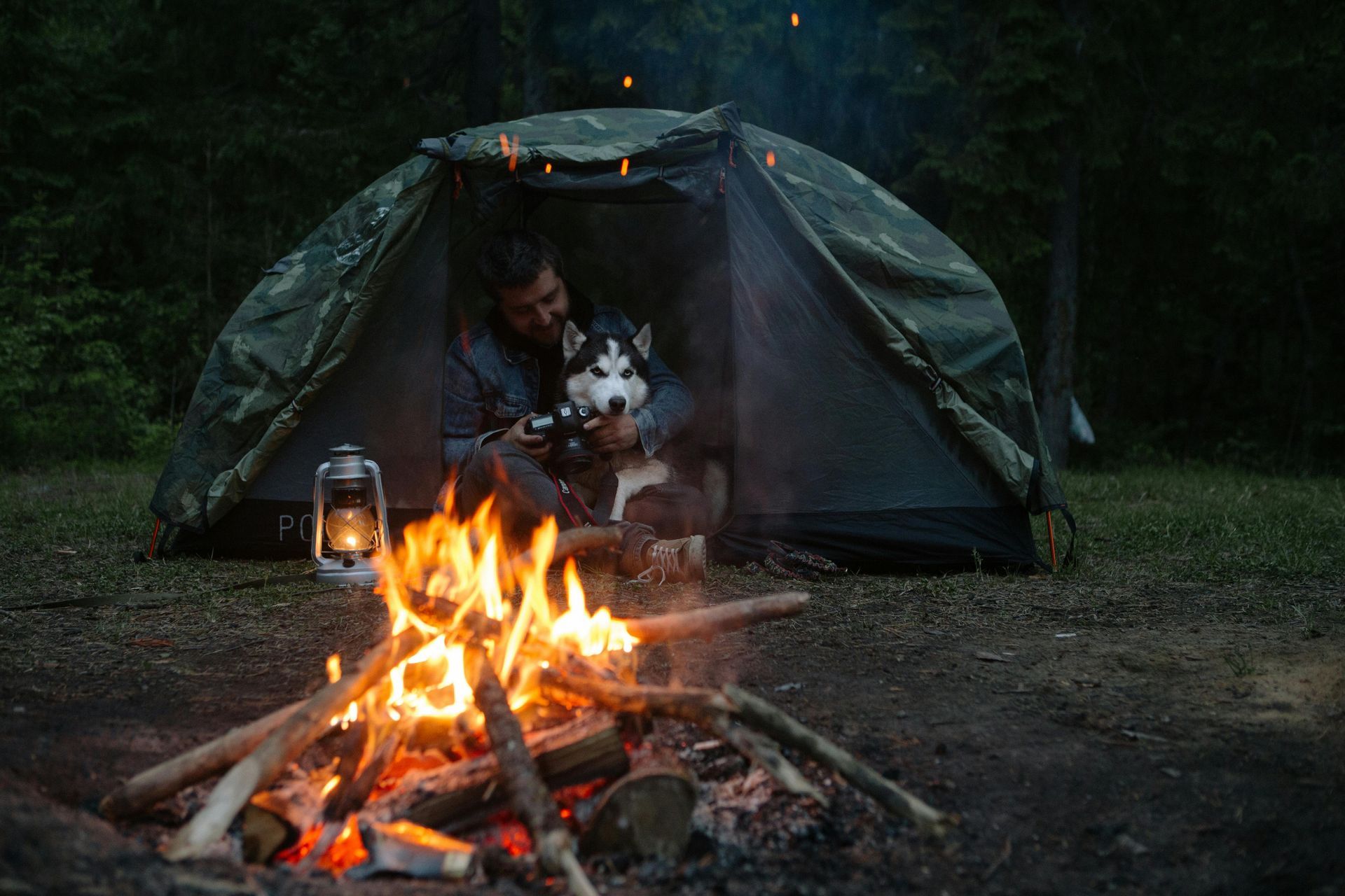 Man and husky dog camping near campfire in a forest at night.