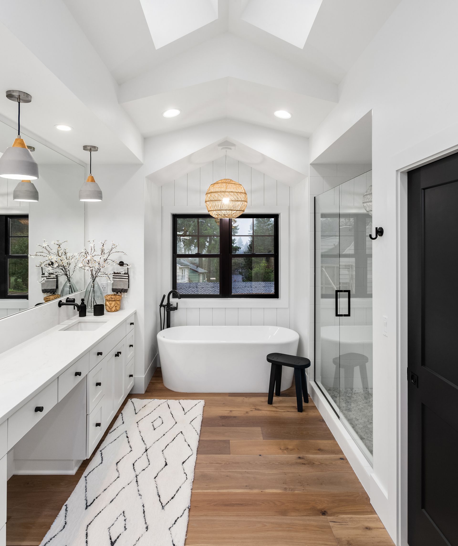 Bright modern bathroom with freestanding tub, glass shower, double vanity, white walls, and wood floor.