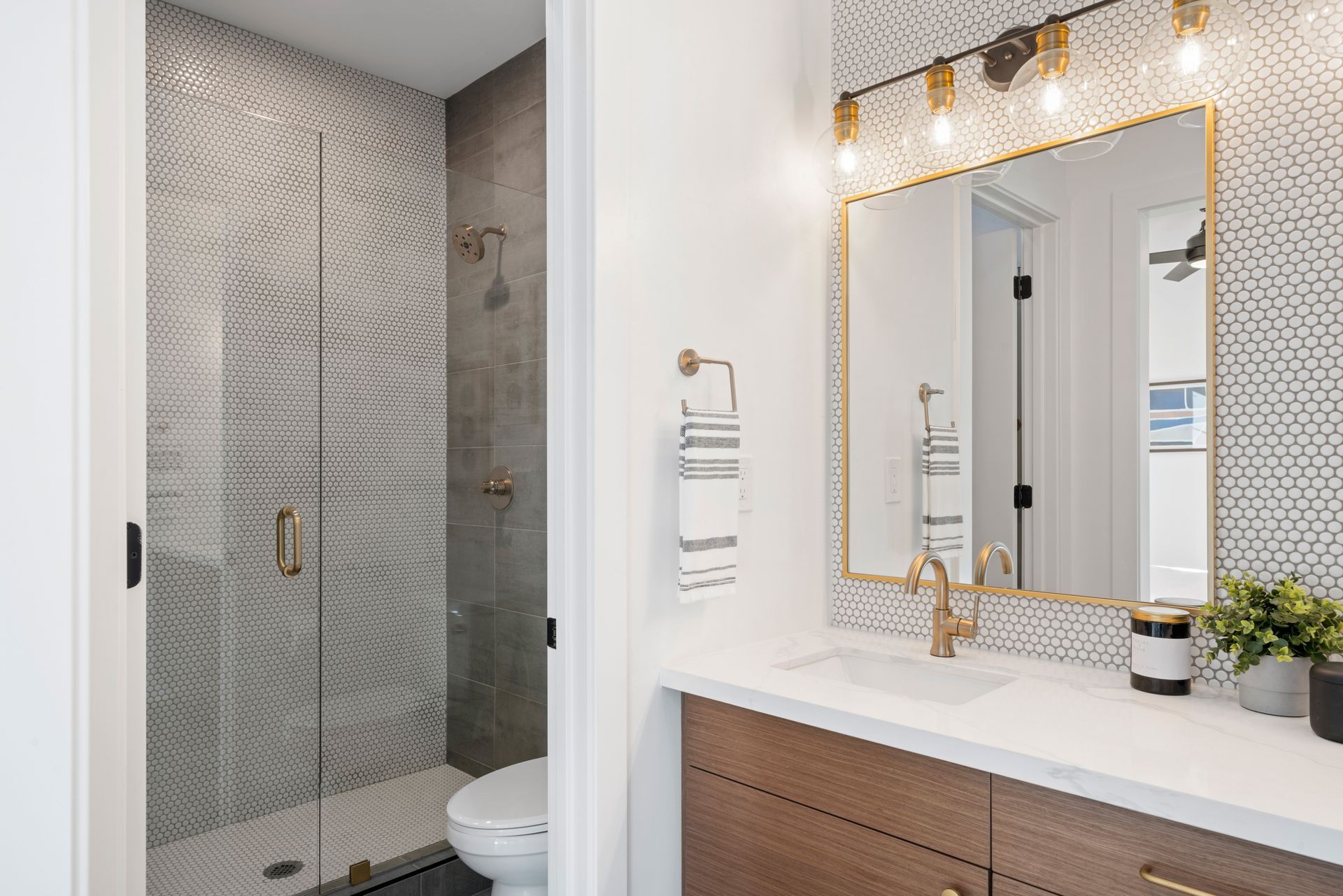 Modern bathroom with a tiled shower, white vanity, gold mirror, and light wood cabinet.