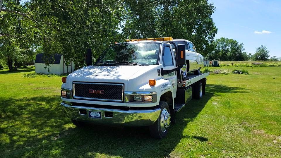 A tow truck is carrying a car on the back of it in a grassy field.