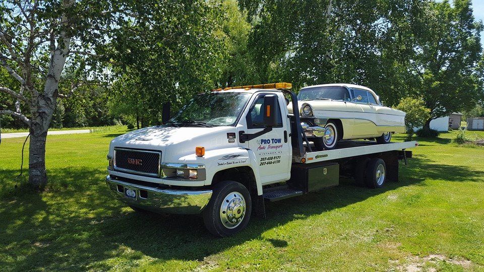 A white tow truck is carrying a white car on the back of it.