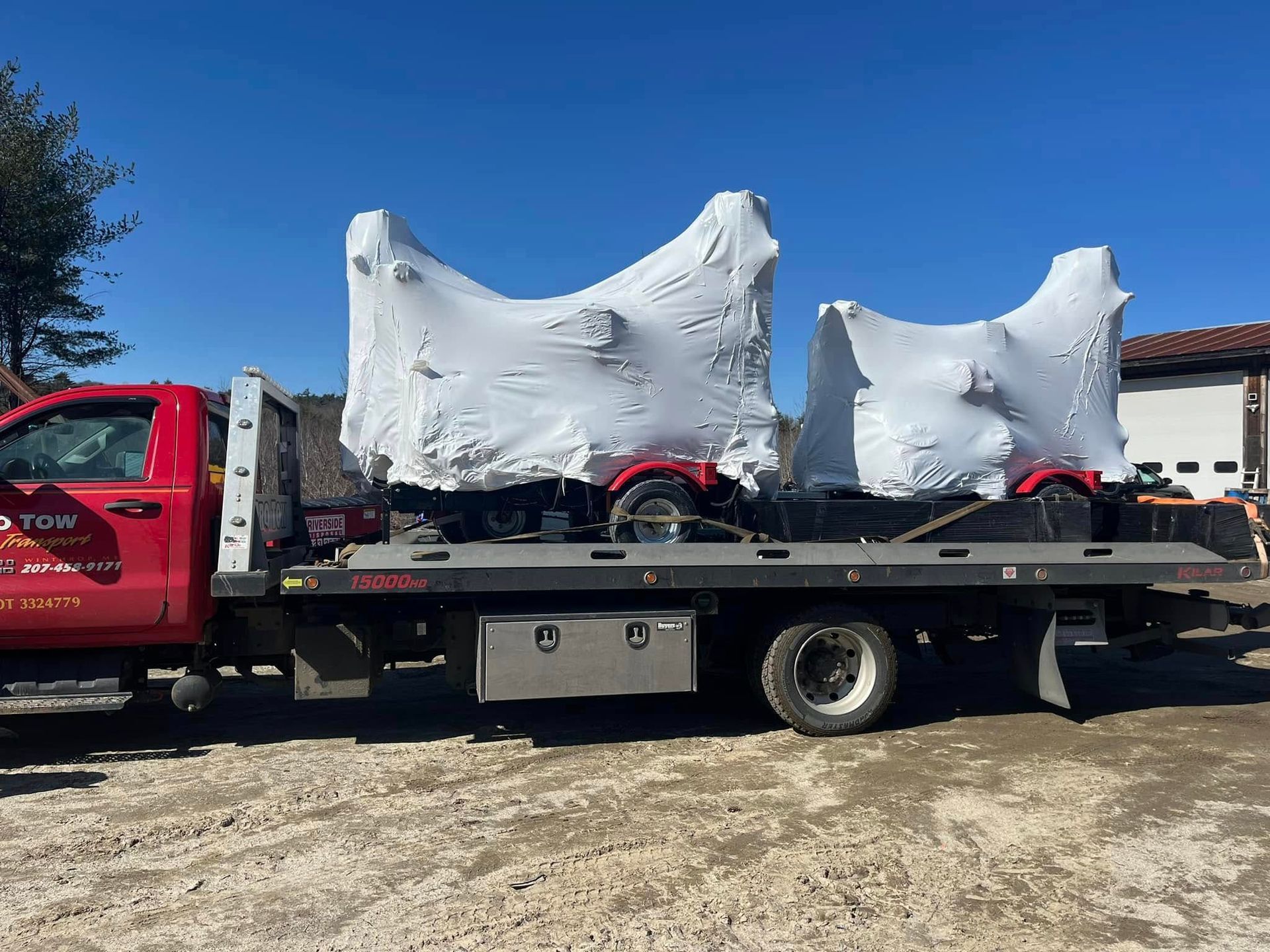 A red tow truck is carrying two atvs wrapped in plastic.