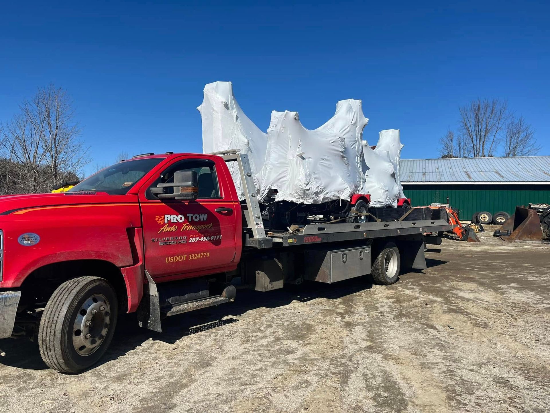 A red tow truck is carrying a large white object on a flatbed trailer.