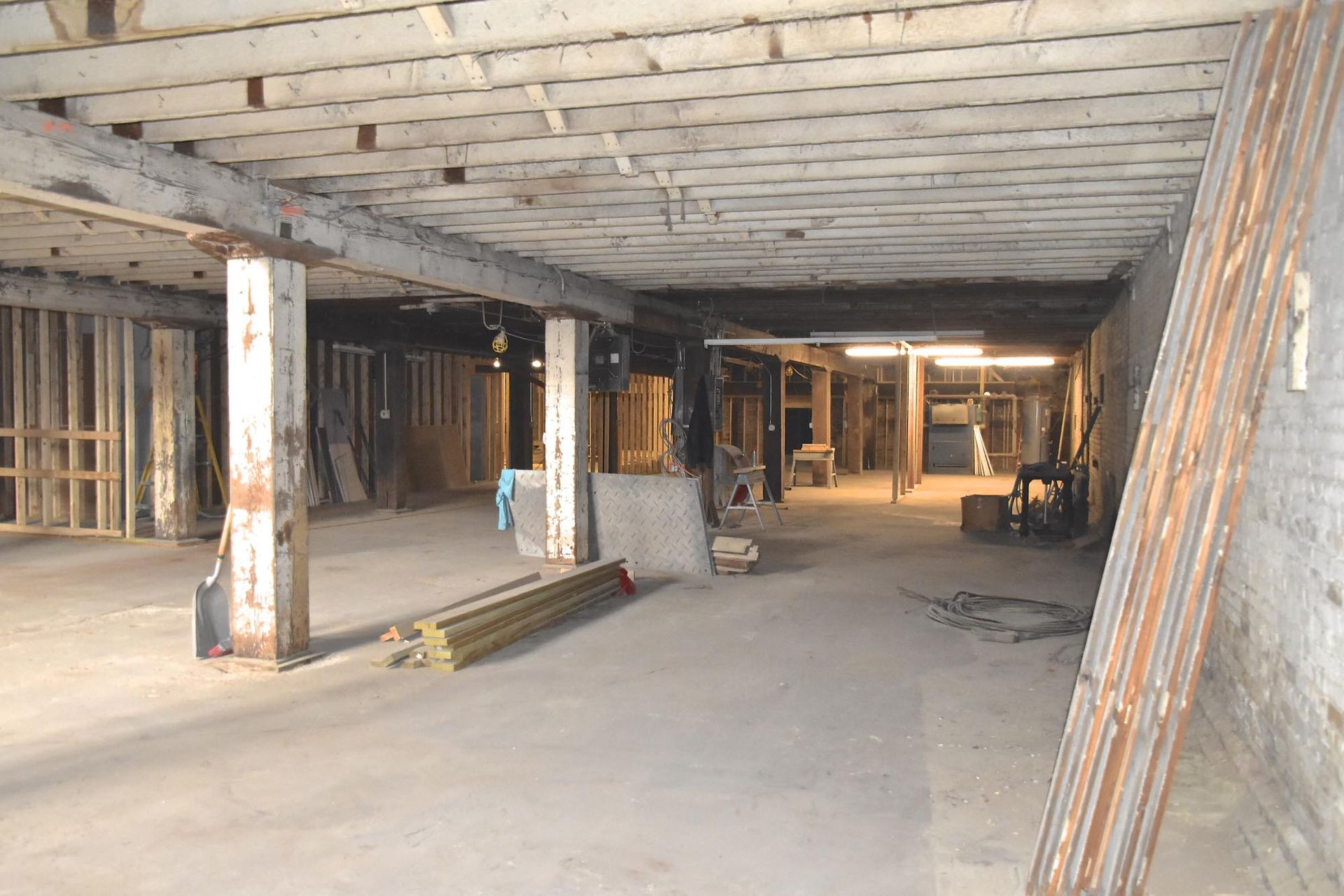 Un cantiere edile al coperto ancora incompiuto, con pavimenti in cemento, travi a vista e colonne portanti.