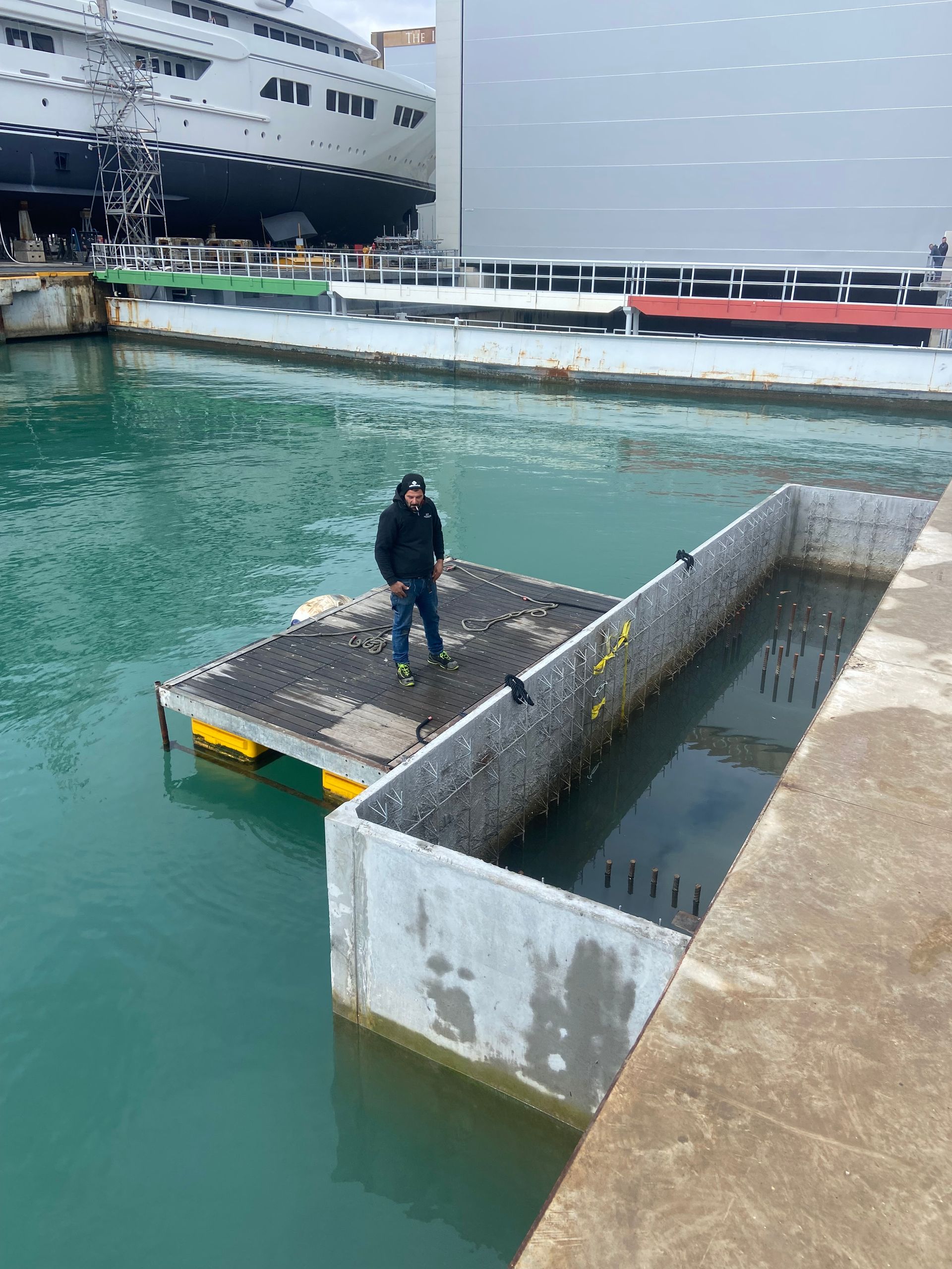 Quattro operai edili con giubbotti di sicurezza arancioni installano un tubo di cemento su un pendio roccioso di montagna, vicino a un escavatore.
