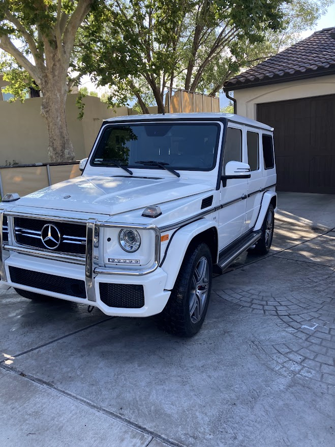 A white mercedes benz g63 is parked in front of a garage.