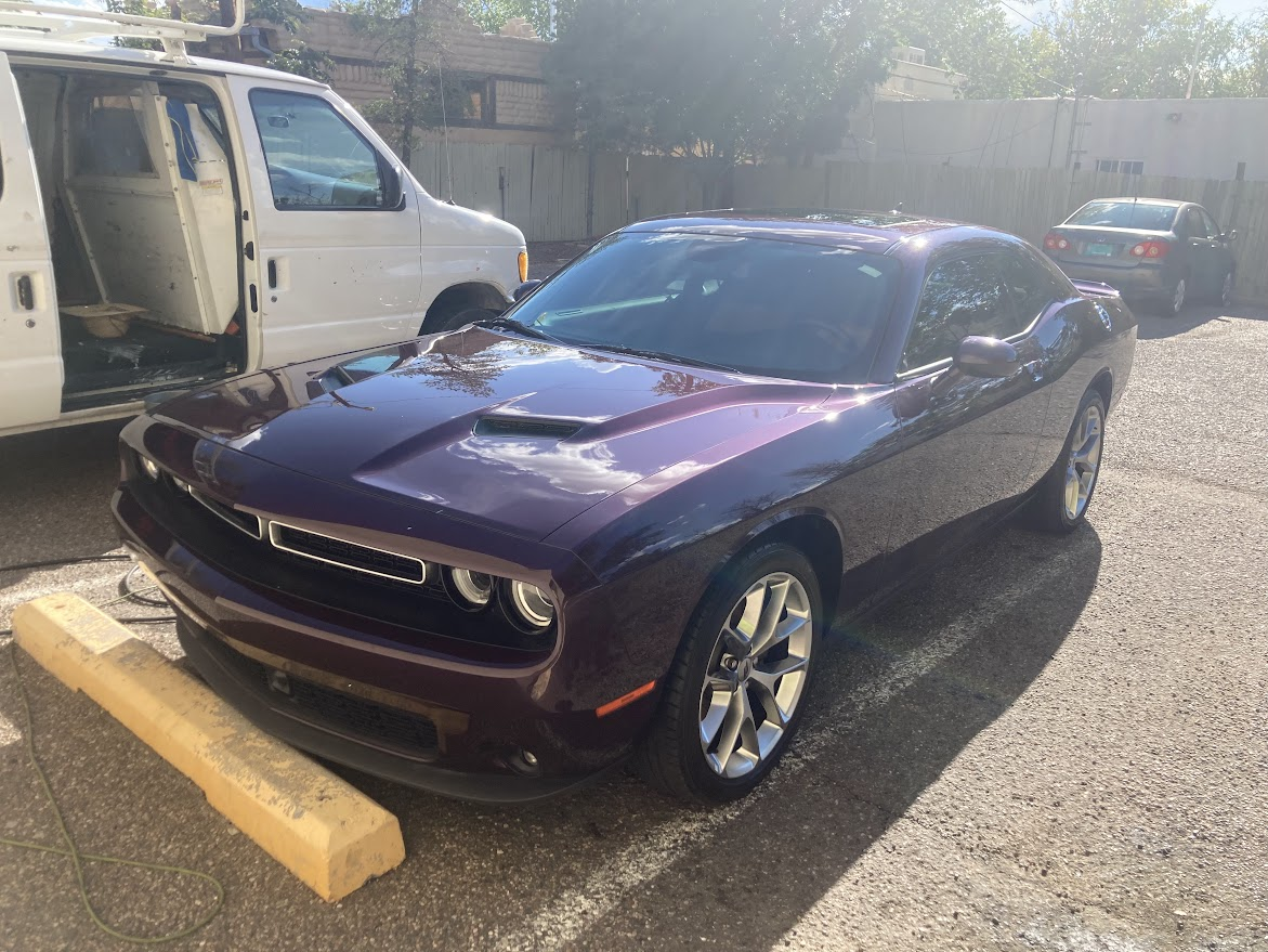 A purple dodge challenger is parked in a parking lot next to a white van.
