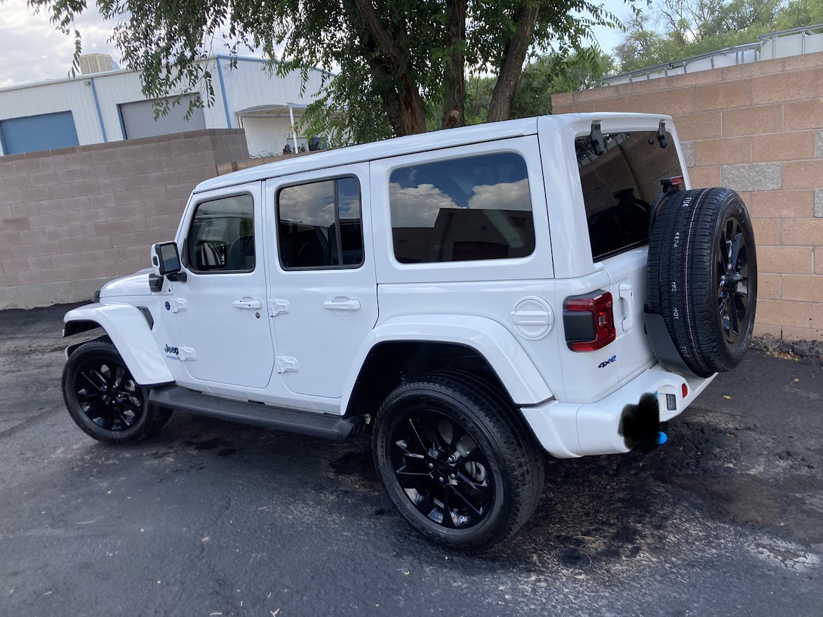 A white jeep is parked in a parking lot next to a tree.