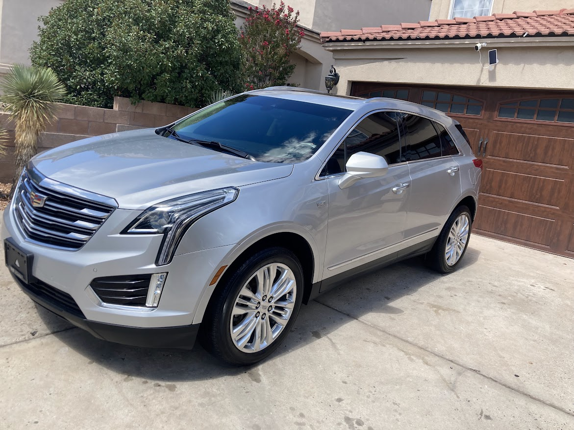 A silver cadillac is parked in a driveway in front of a house.