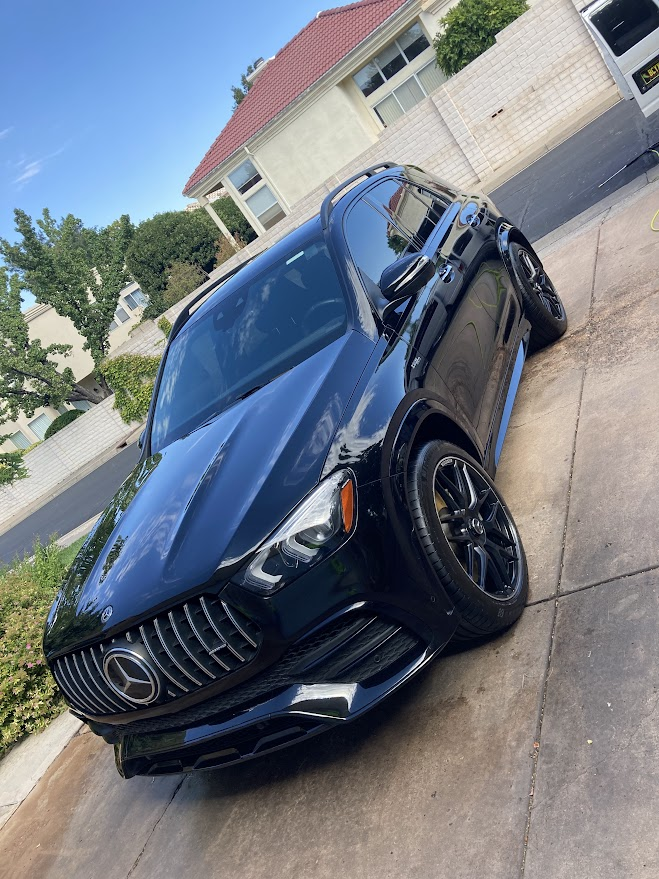 A black car is parked on the side of the road in front of a house.