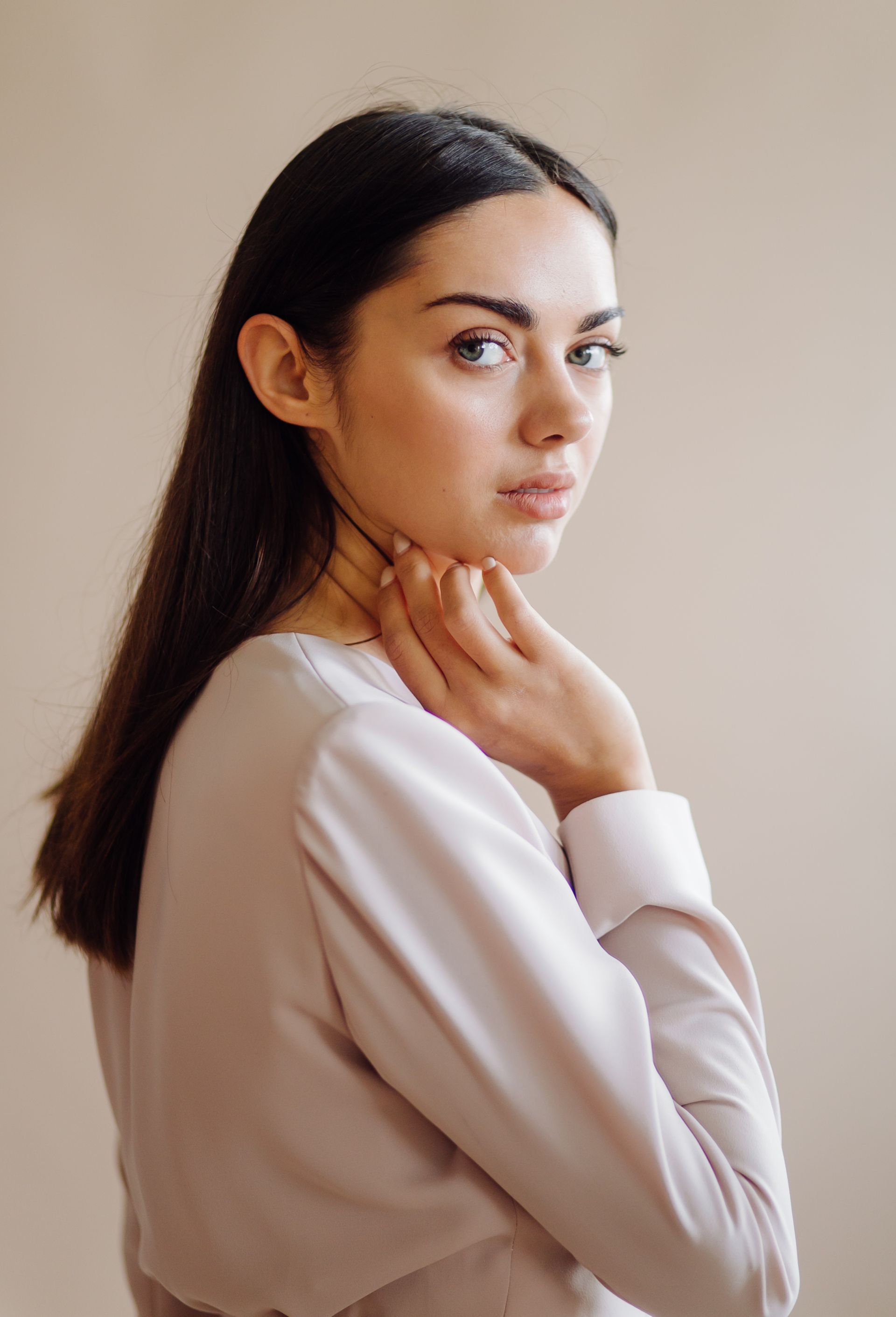 A woman in a white shirt is holding her neck and looking at the camera.