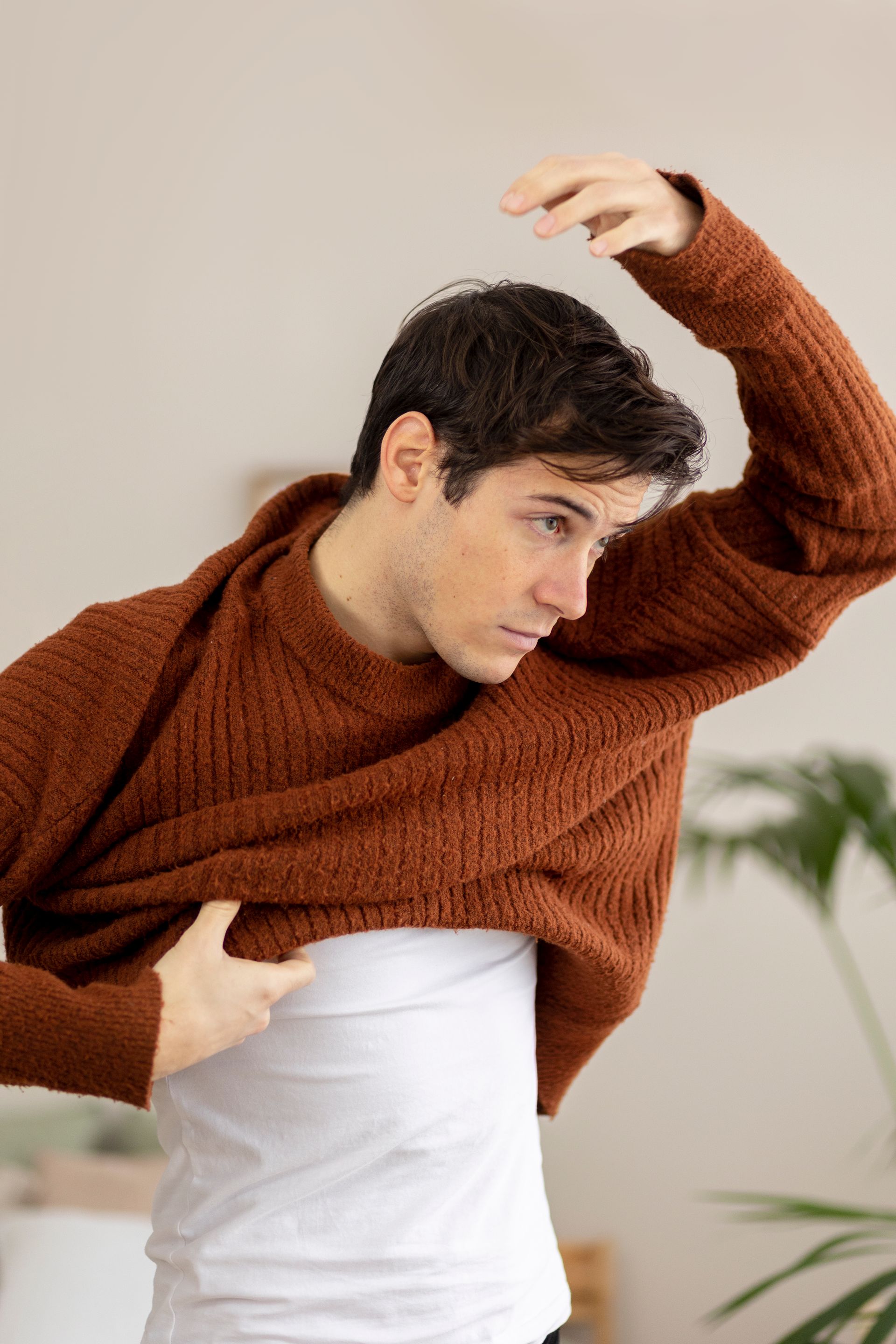 A young man is wearing a brown sweater and a white shirt.