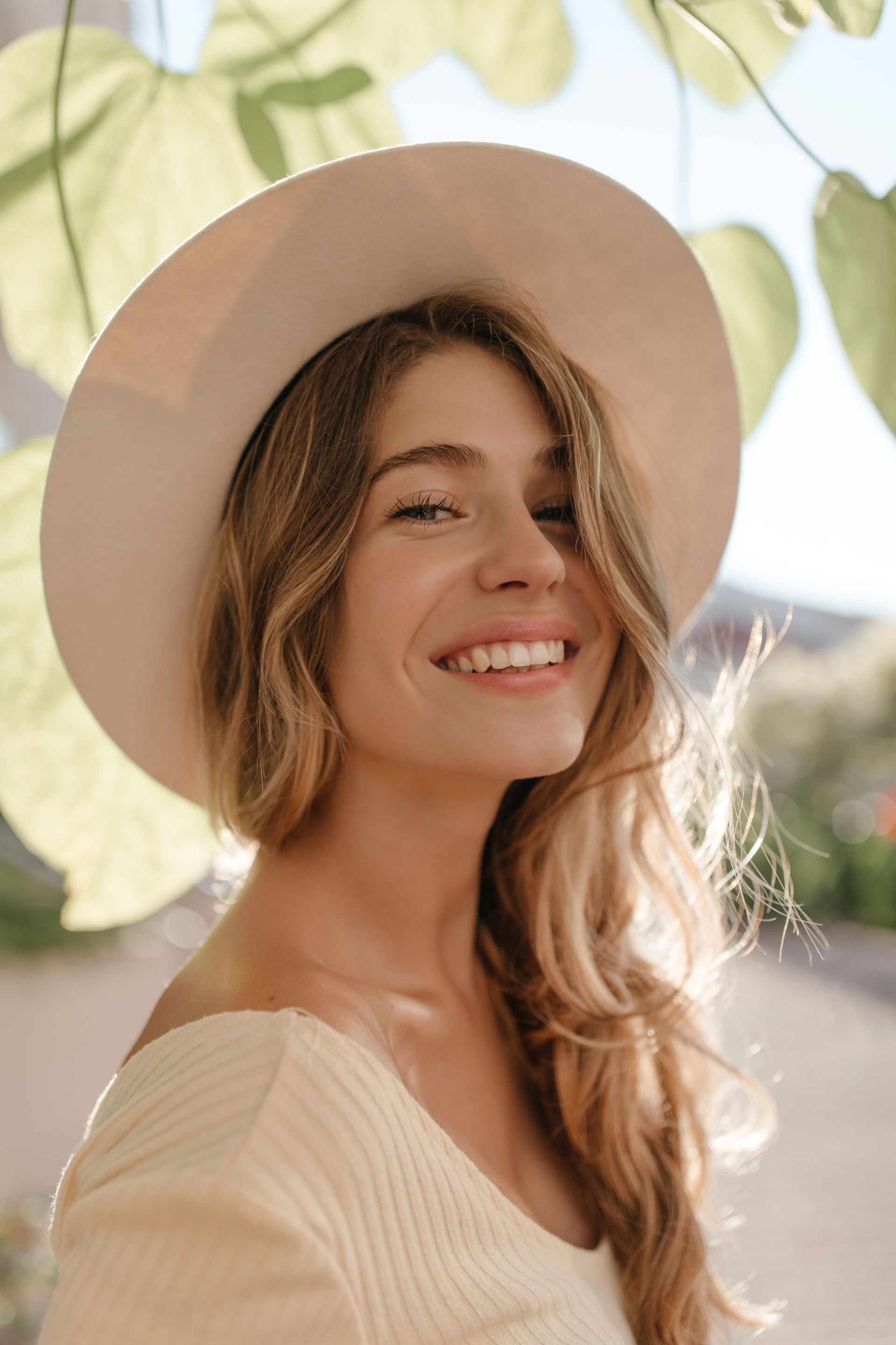 A woman wearing a white hat and a white sweater is smiling.