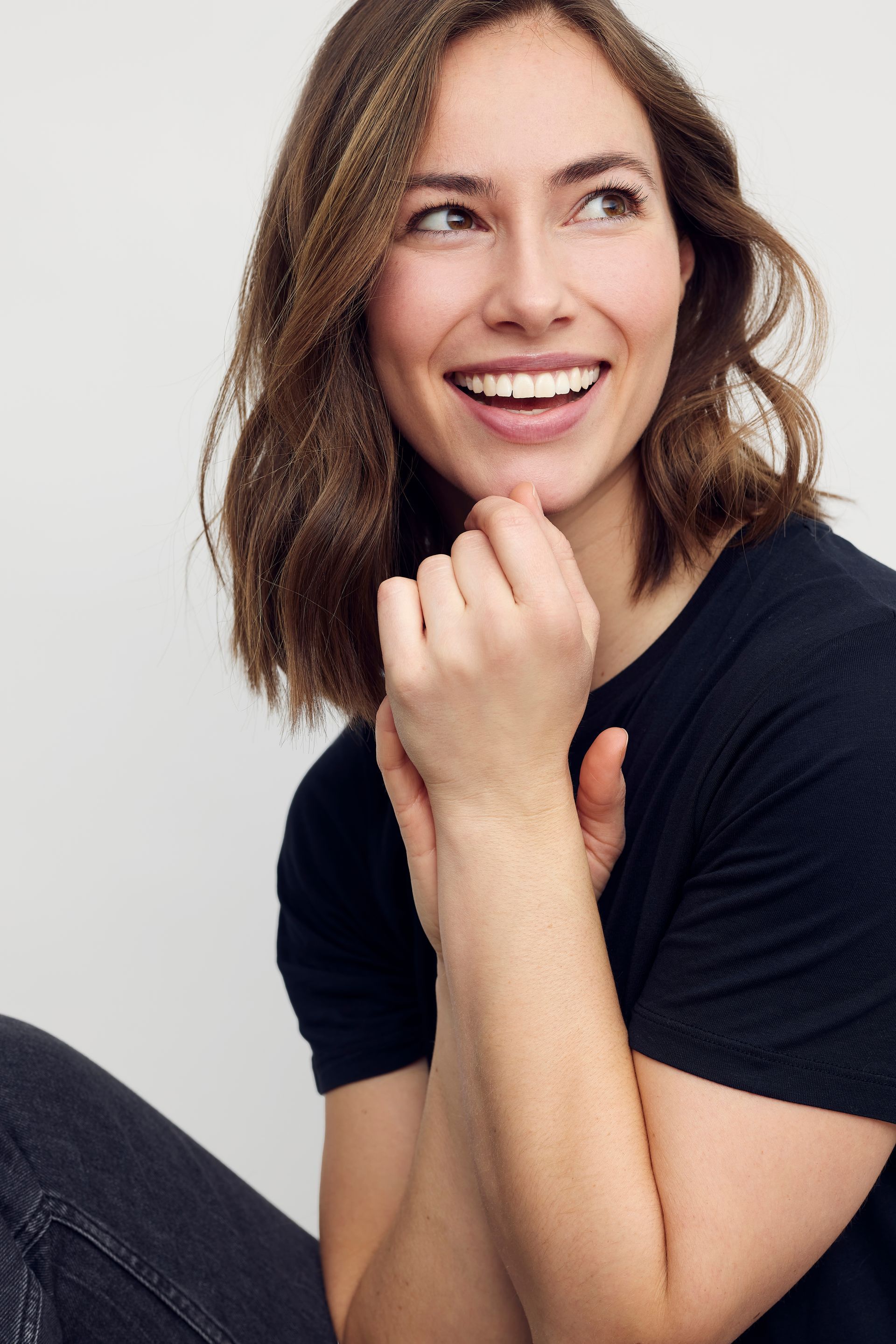 A woman in a black shirt is smiling with her hands on her chin.