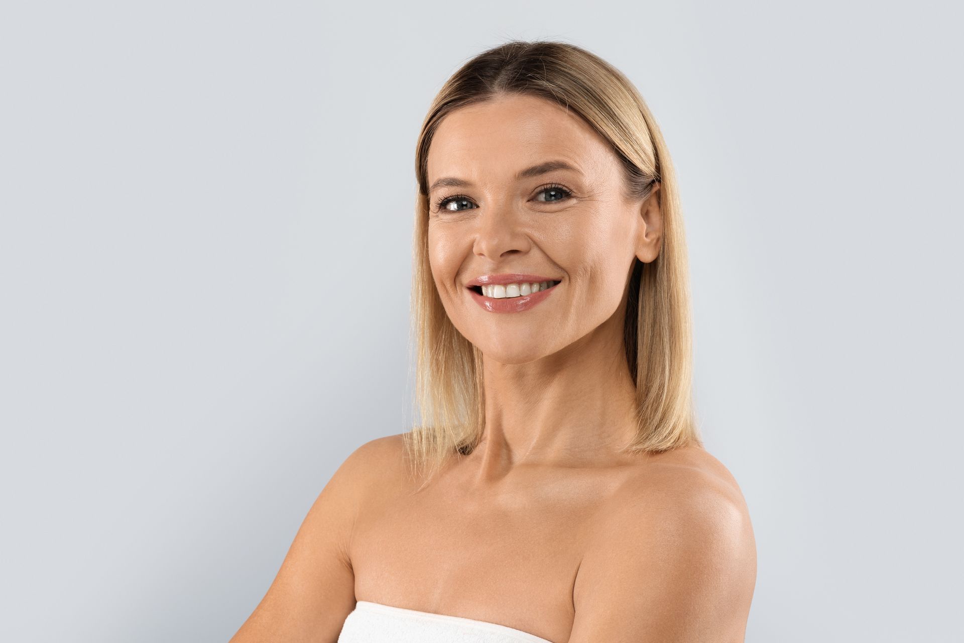 A woman is smiling and looking at the camera while wearing a white towel.