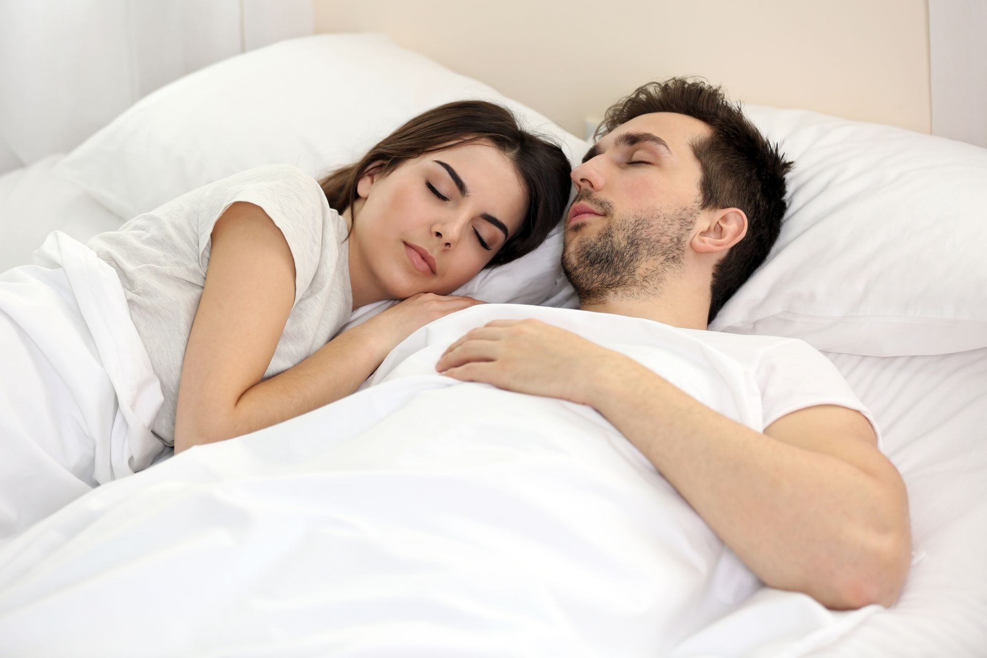 A man and a woman are sleeping next to each other in a bed.