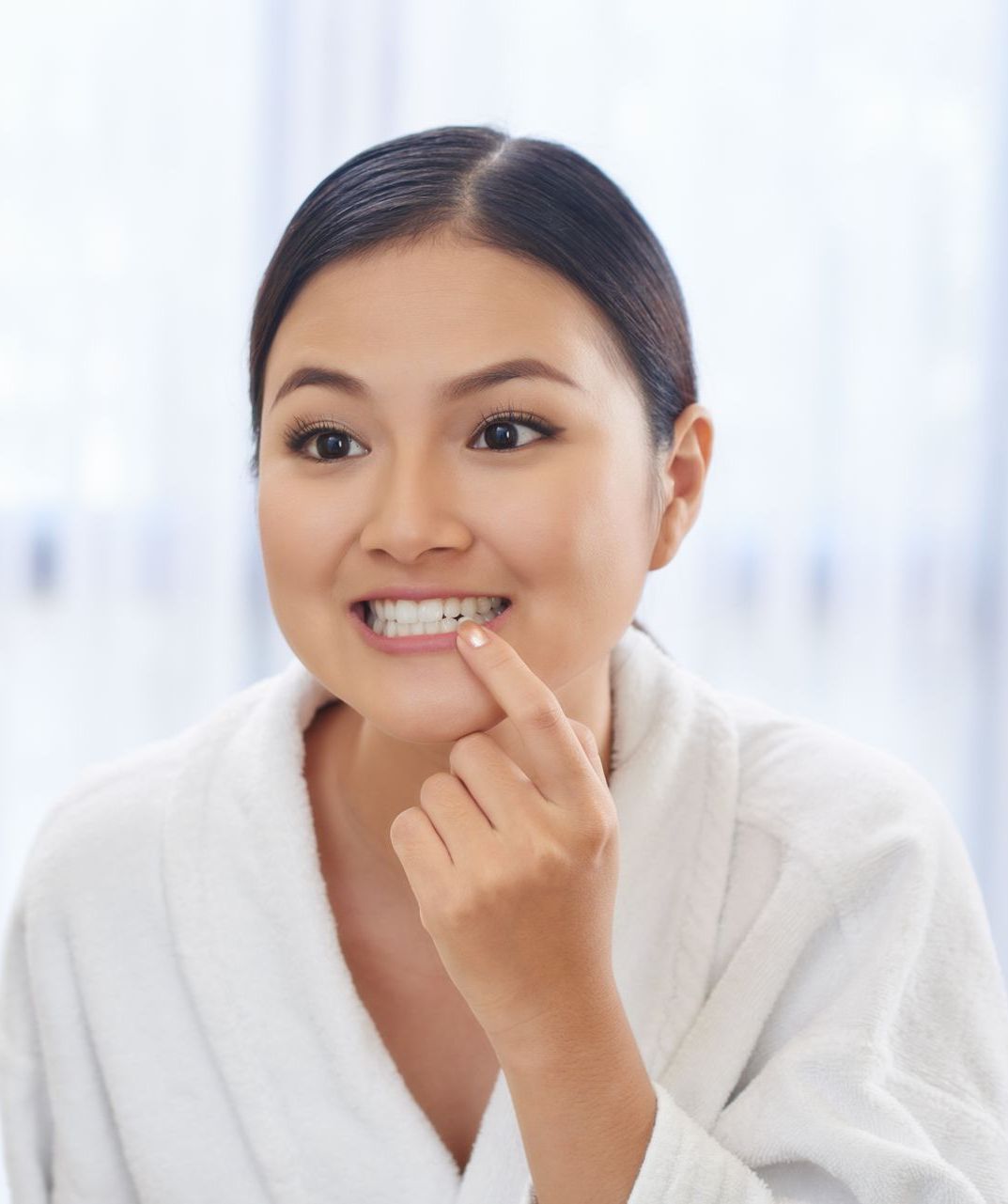 A woman in a bathrobe is smiling and pointing at her teeth.