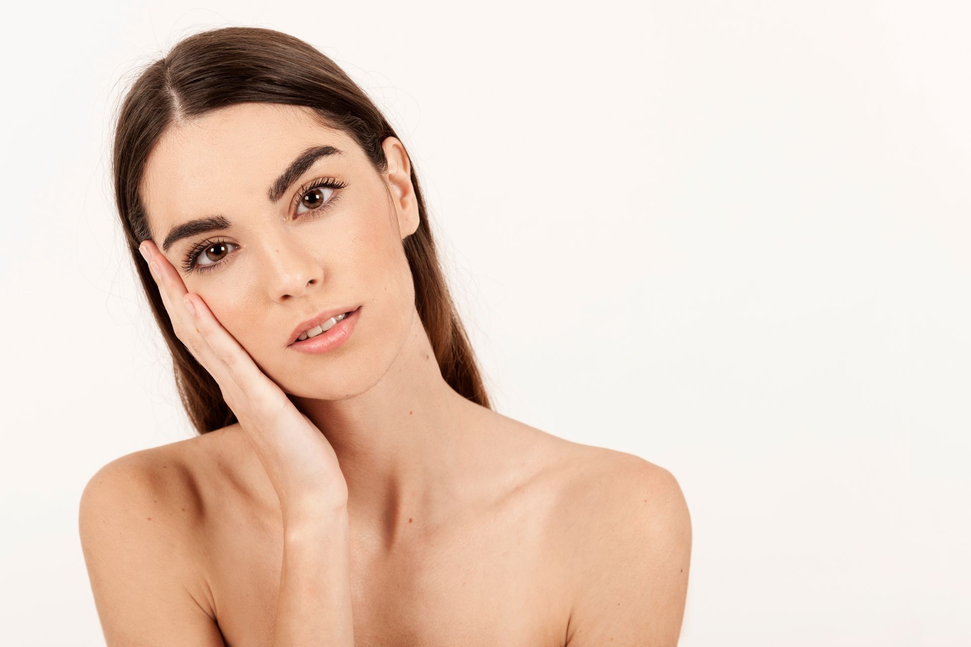 A woman is touching her face with her hand and looking at the camera.