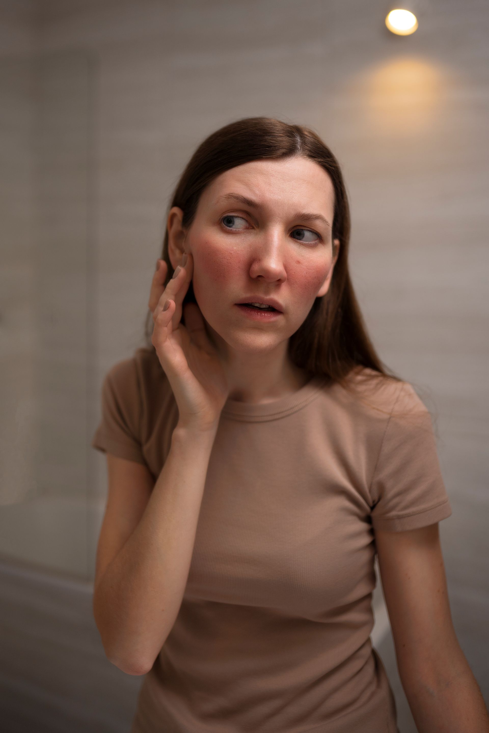 A woman with red spots on her face is looking at herself in the mirror.