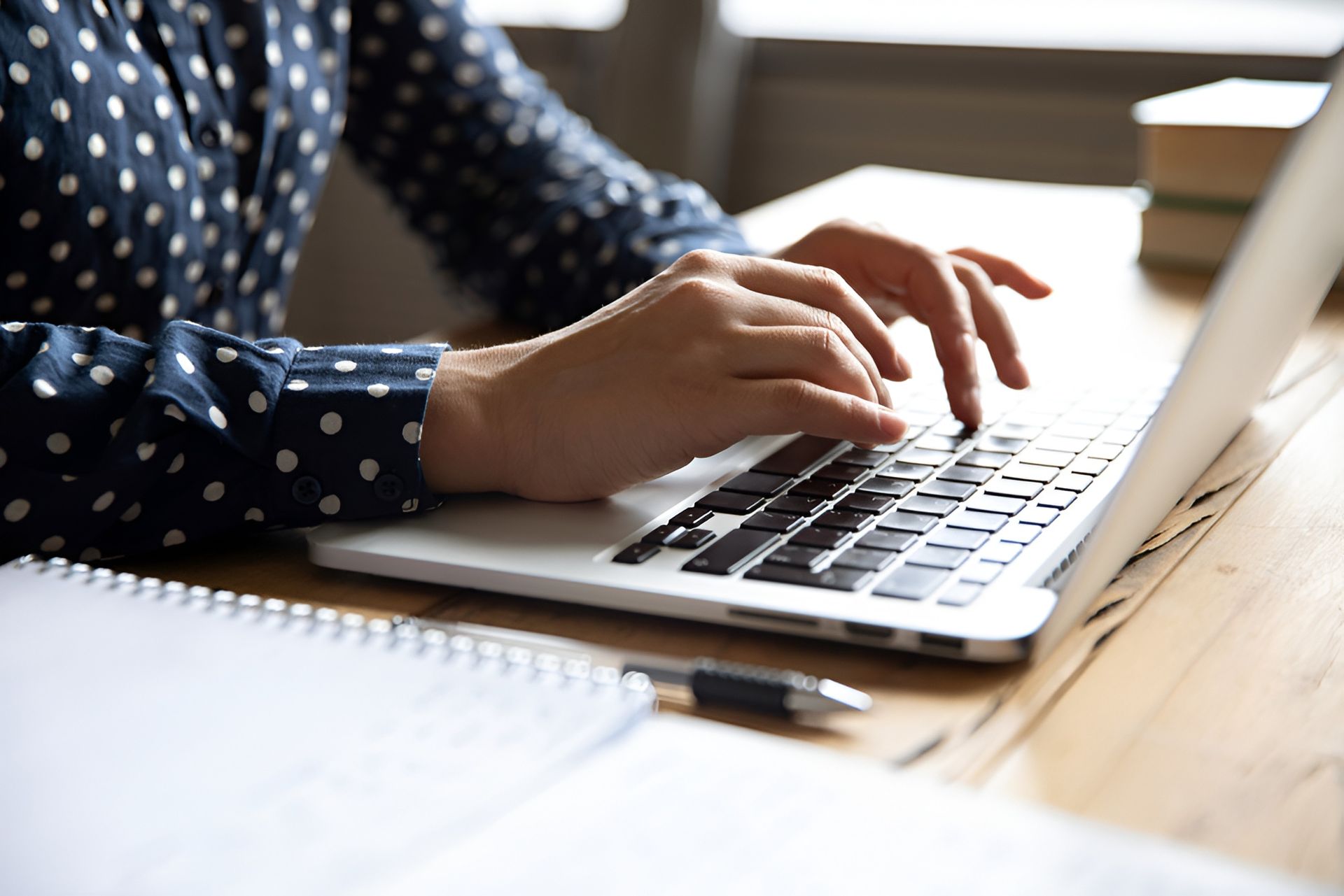 Person Typing on a Laptop at a Wooden Desk With a Notebook and Pen — Allquip Rentals Pty Ltd in Cooroy, QLD