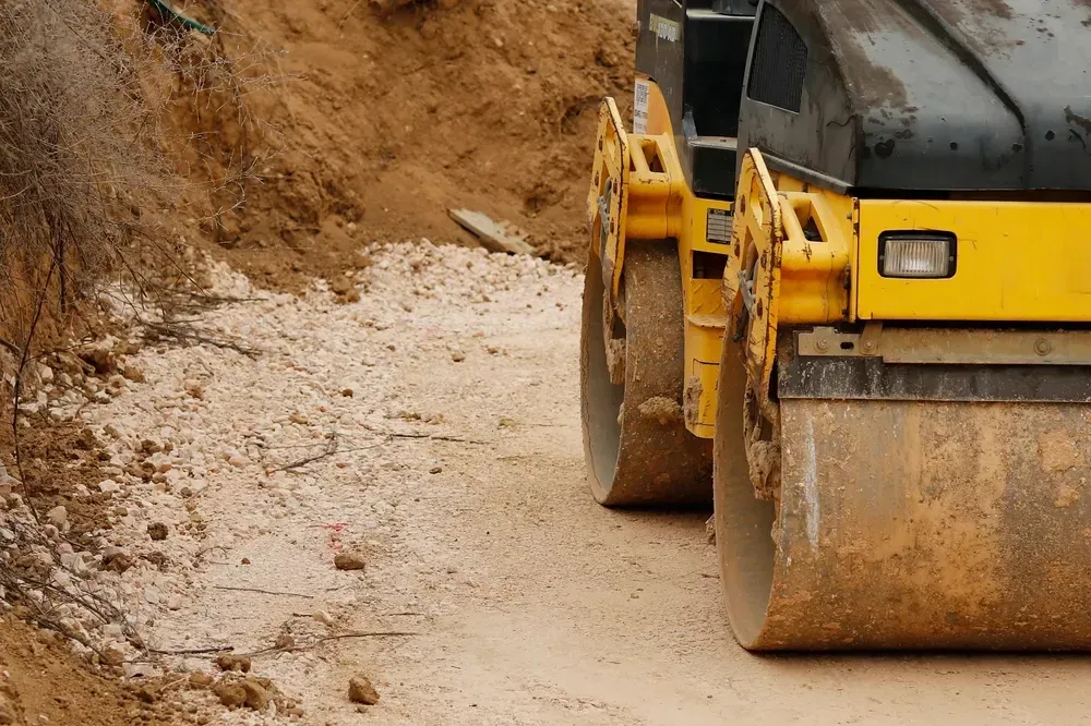 Road roller compacting gravel on a dirt road. Yellow machine, brown soil. — Allquip Rentals Pty Ltd in Cooroy, QLD