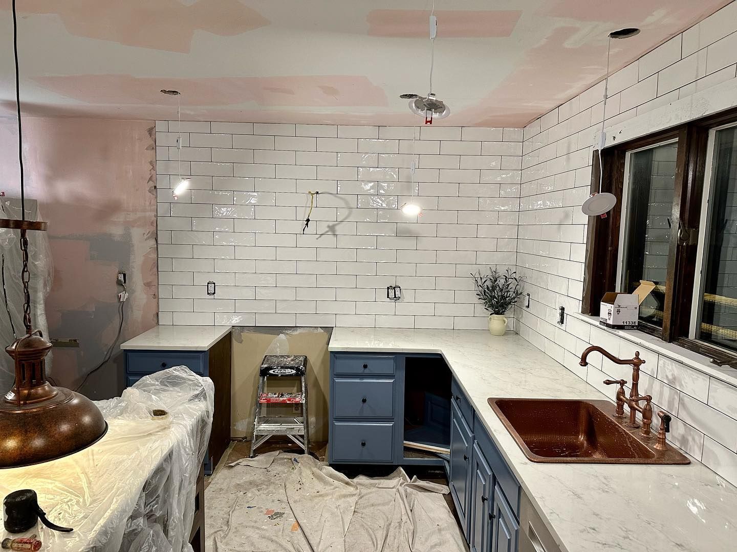 A kitchen is being remodeled with white brick walls and a copper sink.